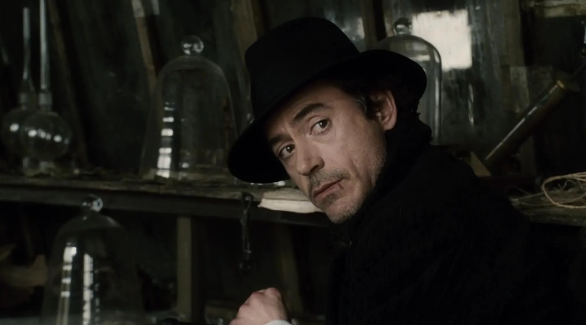 Robert Downey Jr. as the character, Sherlock Holmes, looking disheveled with dark hair and stubble, wearing a rumpled shirt.
