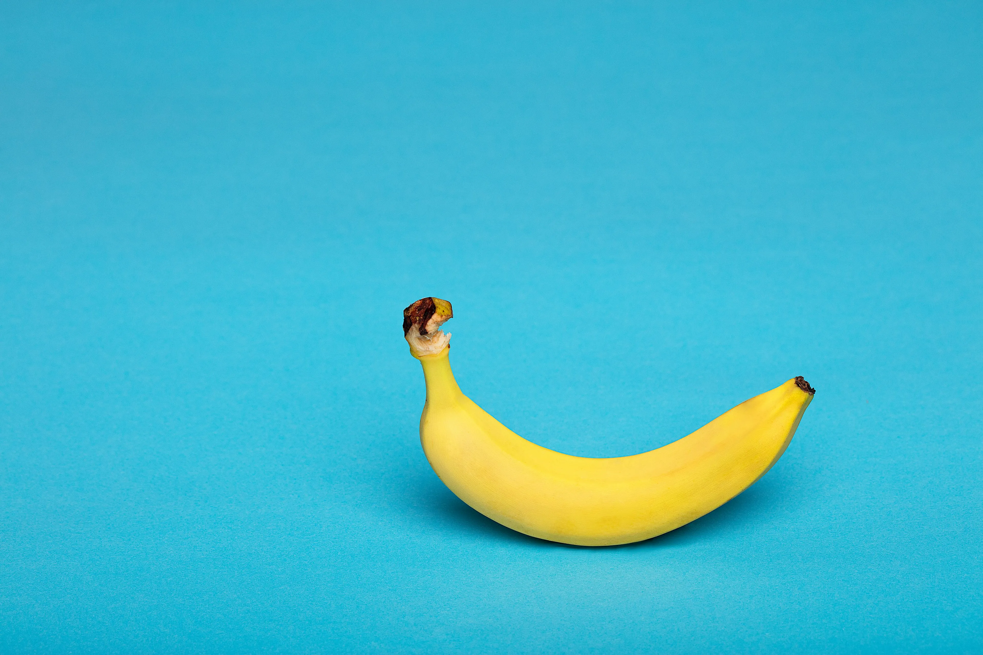 A ripe yellow banana against a teal background, perfect for science trivia about elements like K.