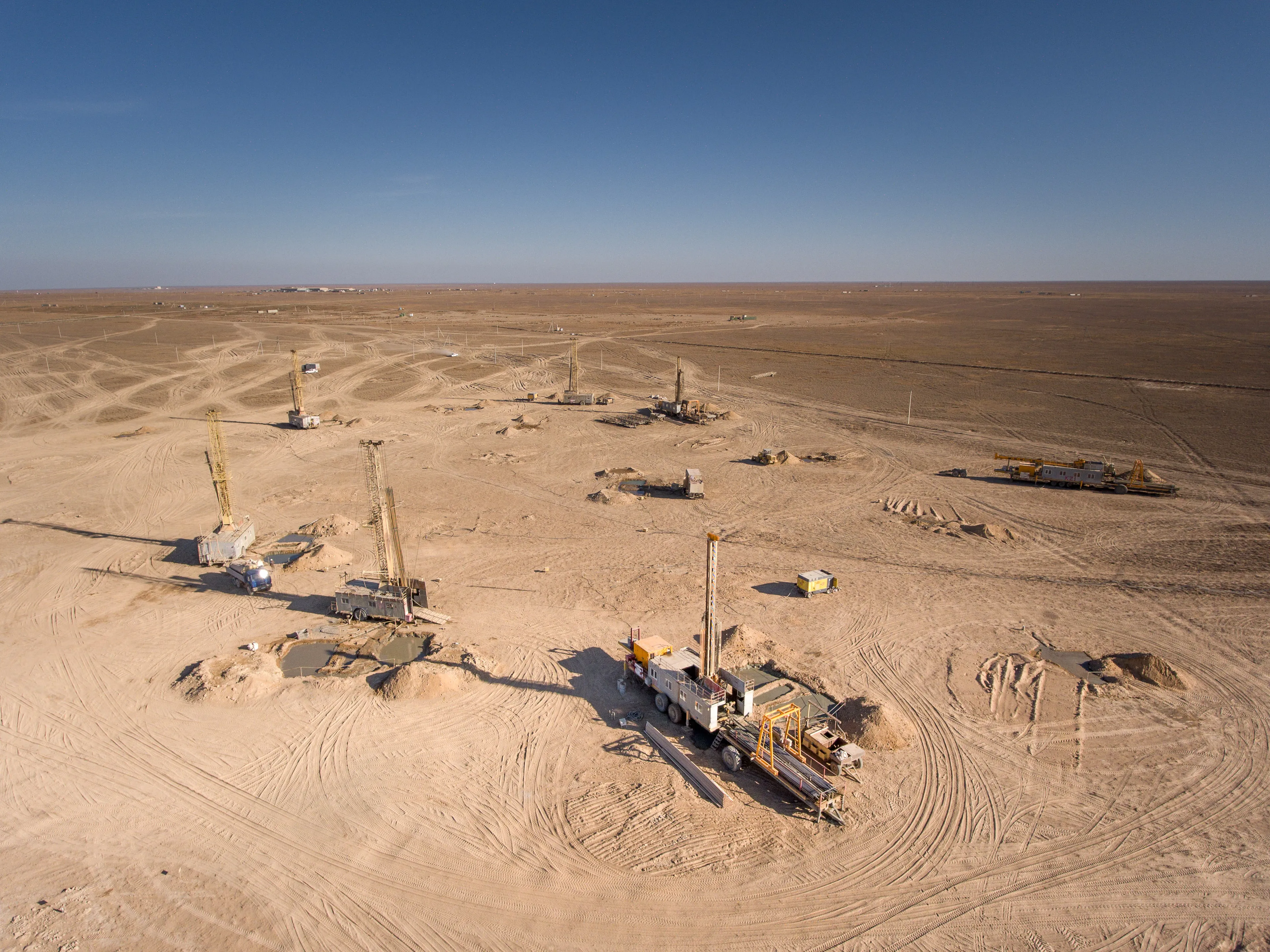 Aerial view of a vast, arid landscape with multiple drilling rigs actively mining for naturally occurring elements.