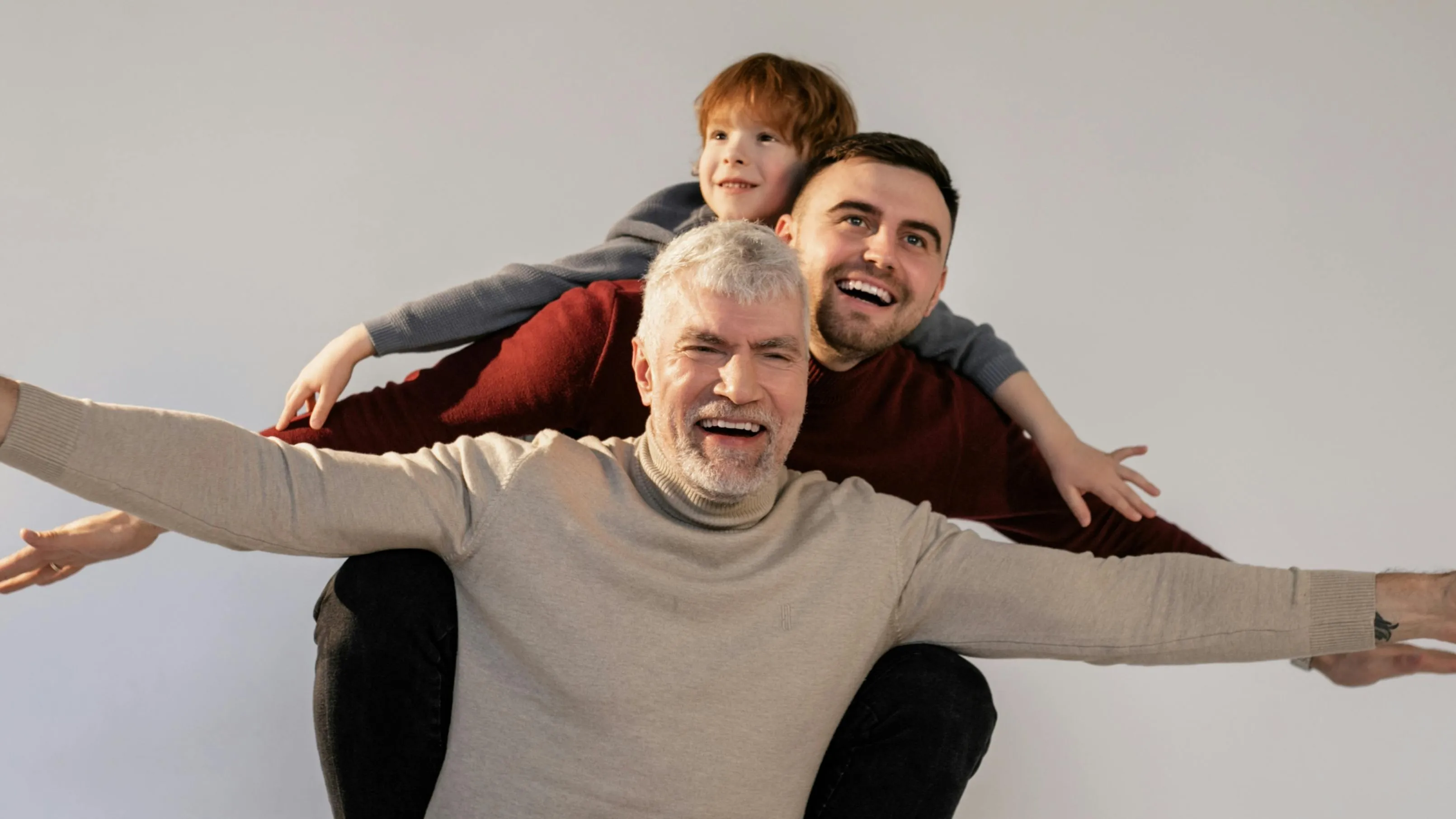 Three generations of males, a grandfather, father, and son, smiling and playfully stacked, symbolizing heredity.