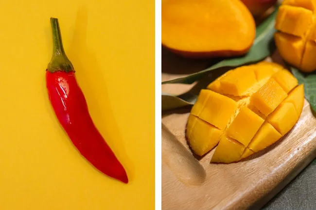 A bright red chili pepper on yellow background next to sliced mango on a wooden board. Candle scent inspiration.