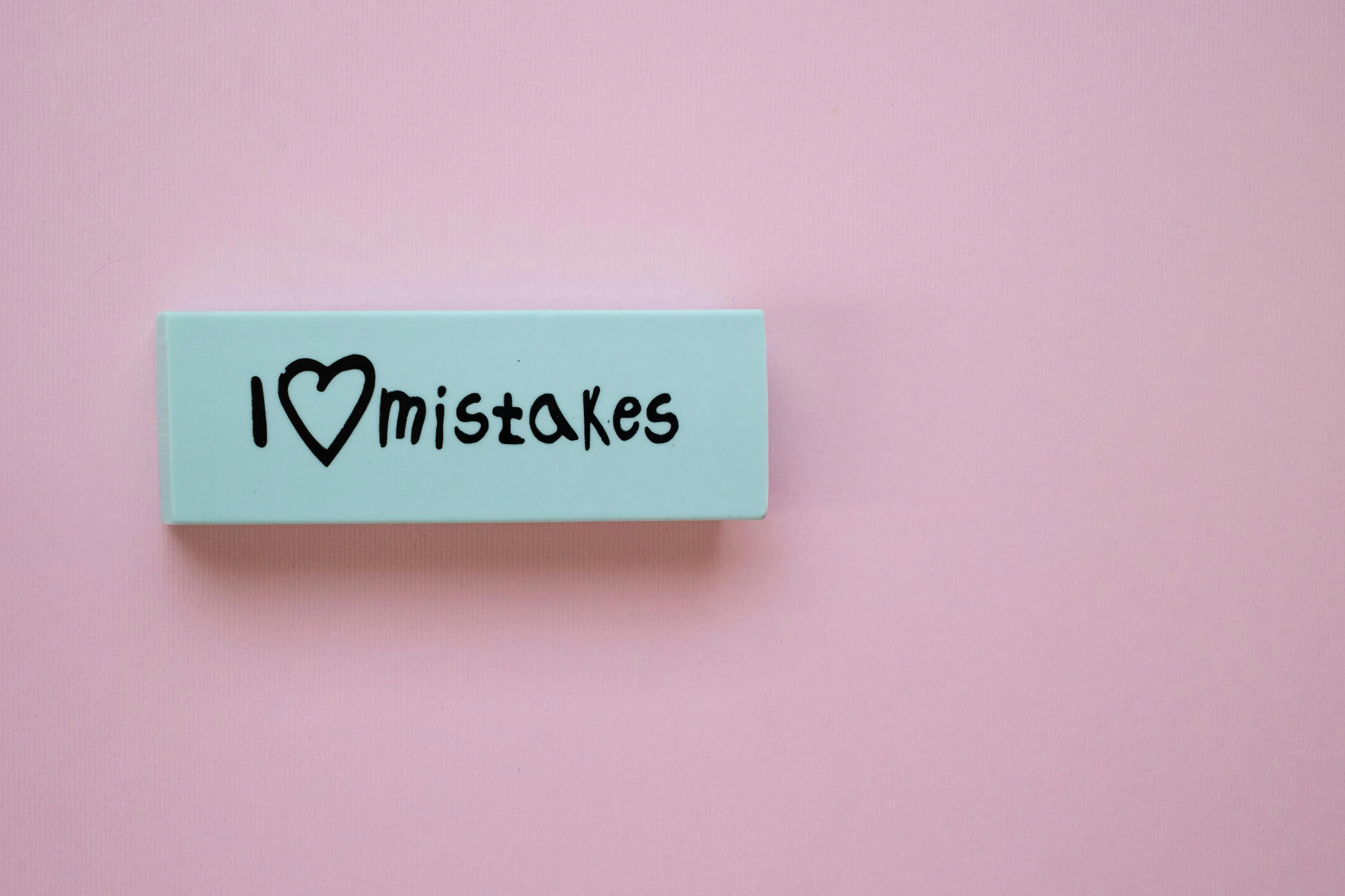 A giant eraser on a pink background, with I ❤️ mistakes written on it. Nostalgic school supply.