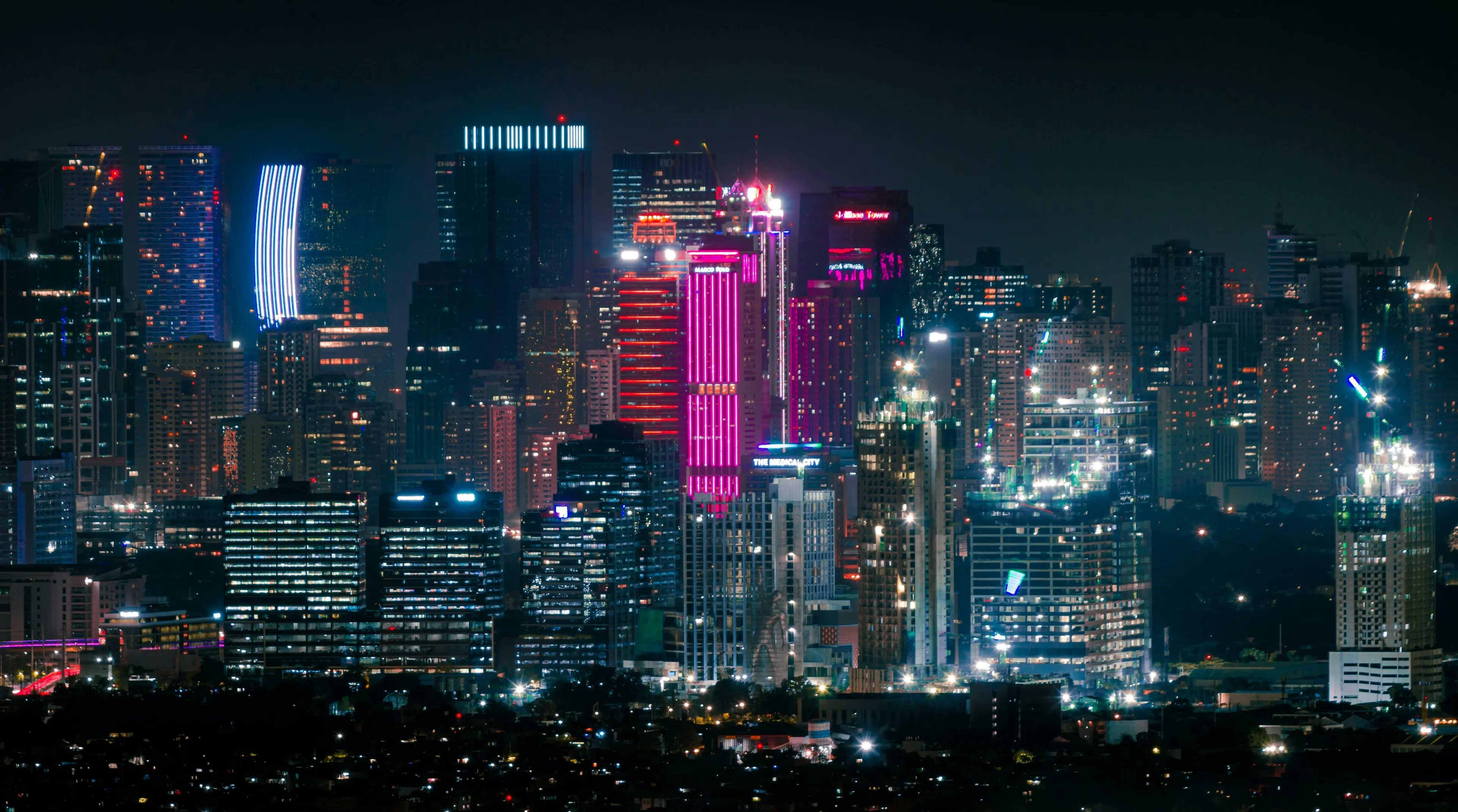 A vibrant night cityscape with skyscrapers illuminated by various colorful lights. Perfect as a desktop wallpaper.