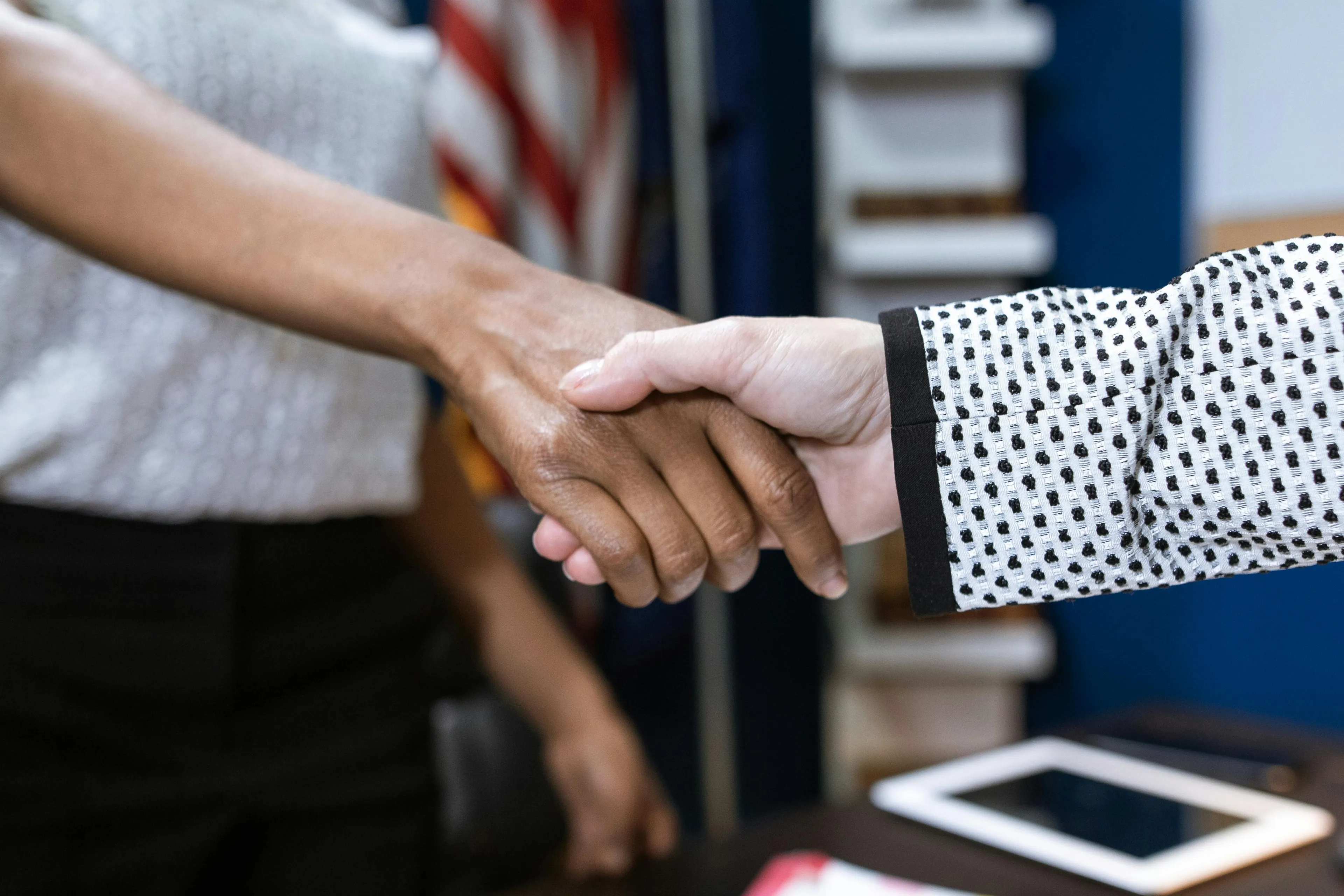 Two women's hands shaking, one dark-skinned, one light-skinned, as a greeting for meeting new coworkers.