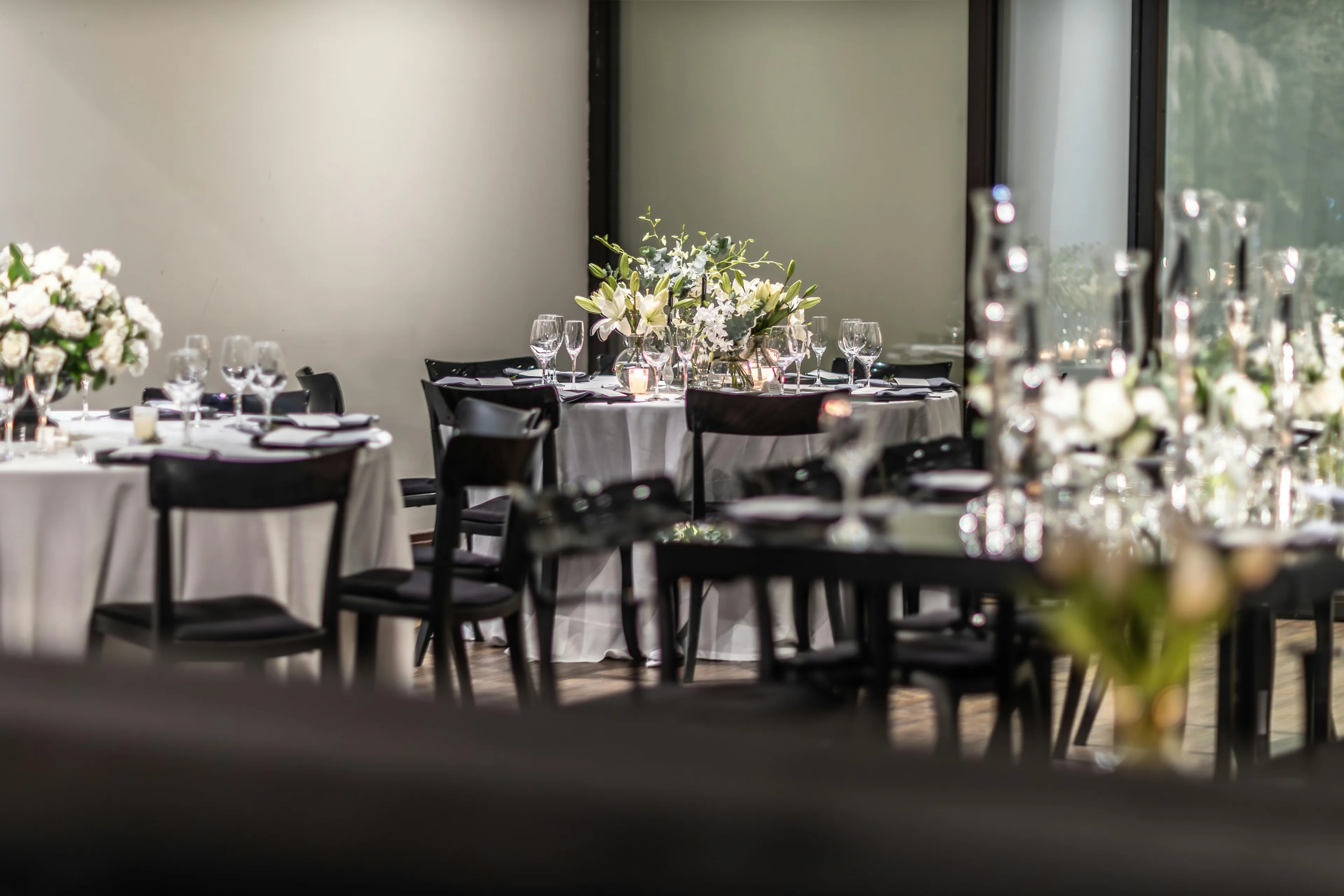 Elegant wedding reception tables with white tablecloths, floral centerpieces, and black chairs. First impression of a luxurious event.