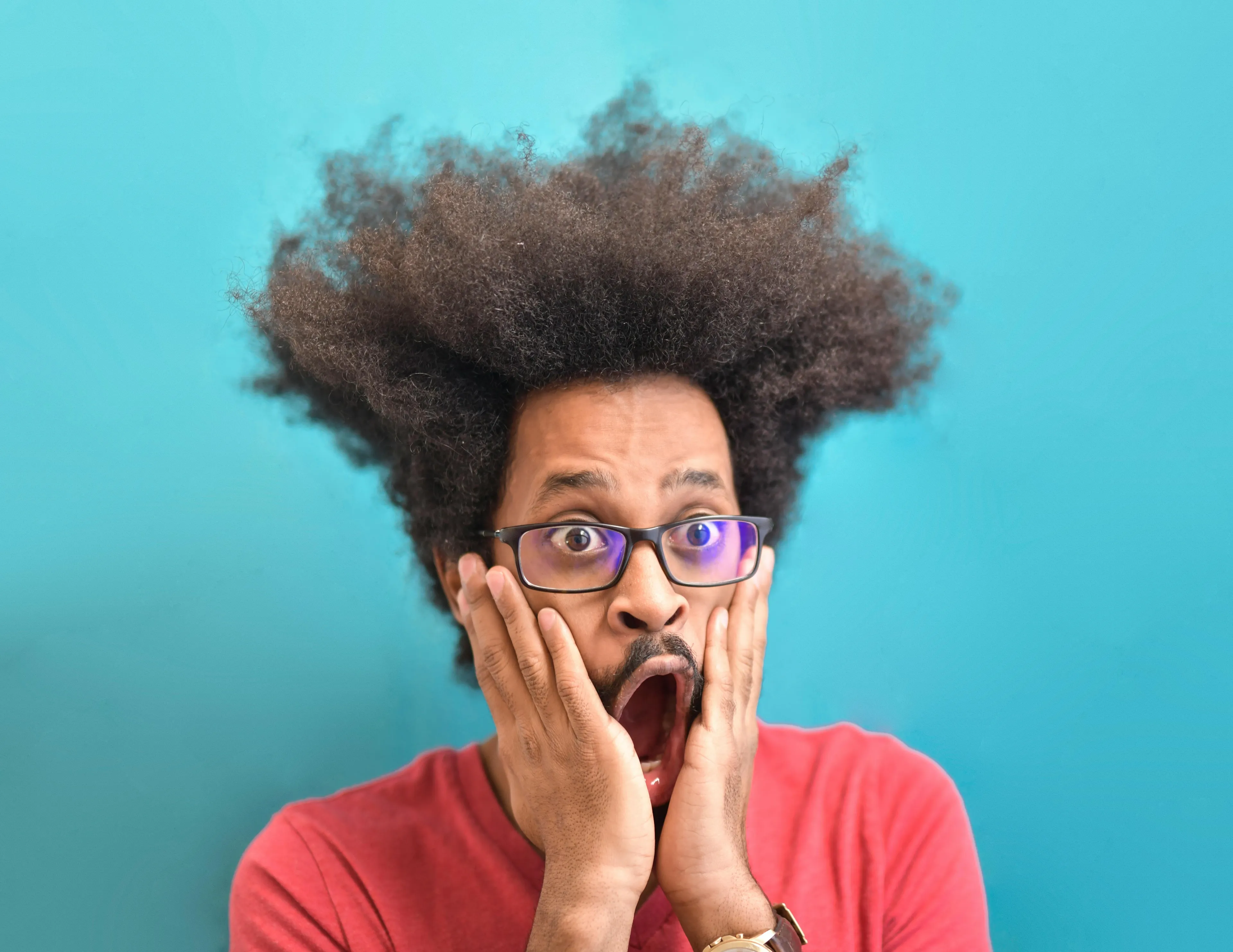 Man with glasses and afro looking shocked against a blue background, expressing first impression and plot twist reaction.
