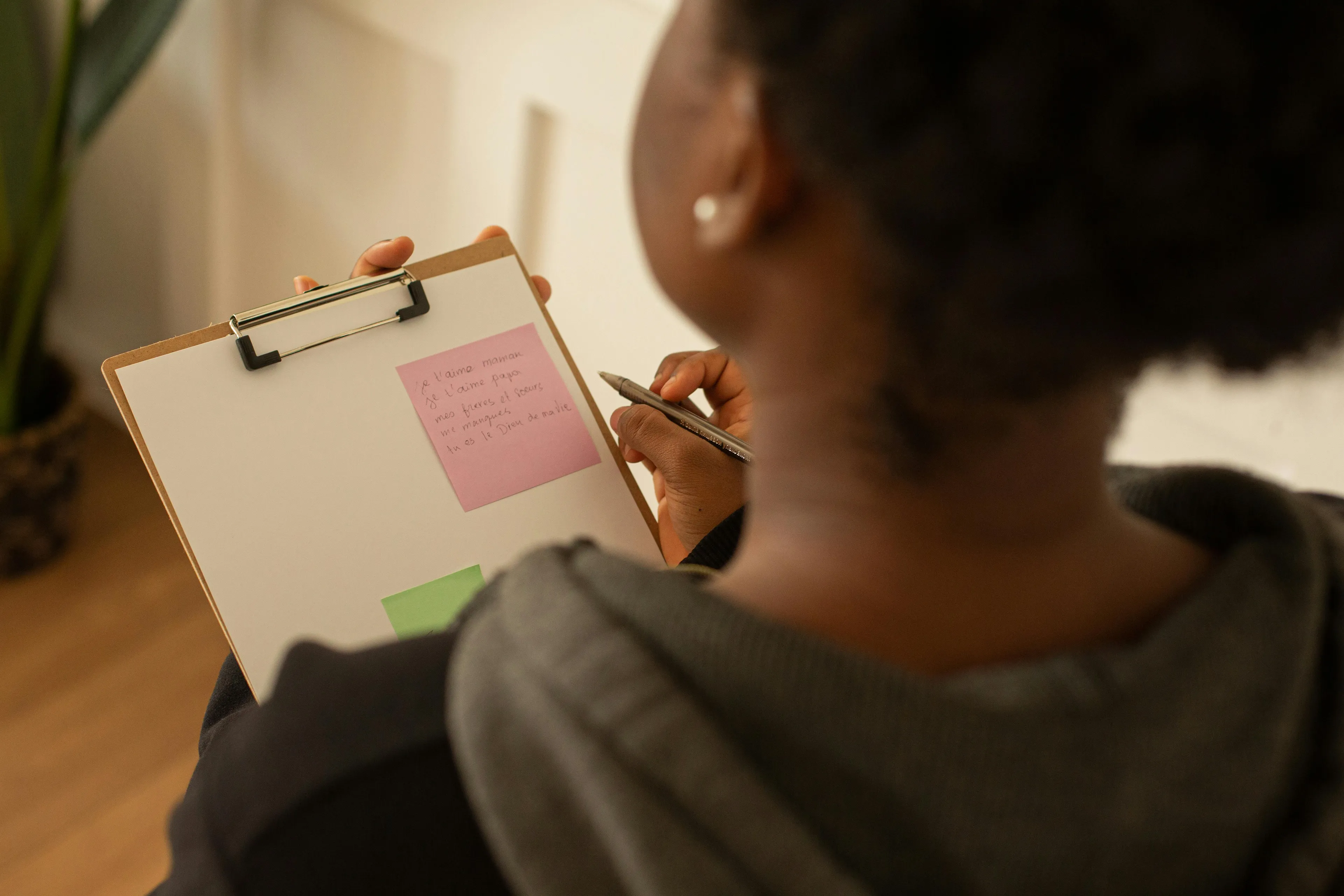 Person from behind writing on a clipboard with pink and green sticky notes, demonstrating their note-taking style.