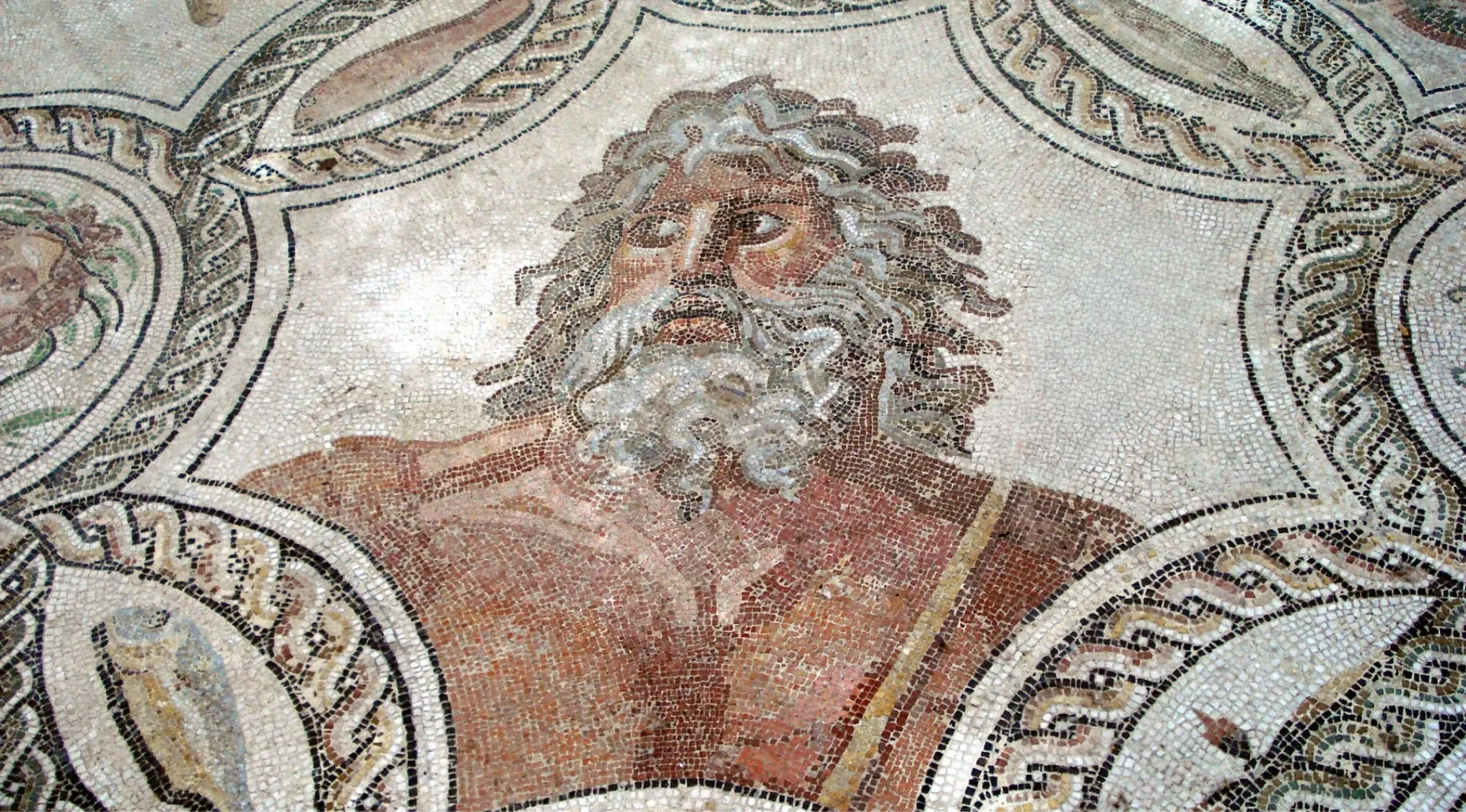 Ancient Greek Mythology mosaic depicting a figure with a beard and wild hair, possibly Poseidon, god of the sea.