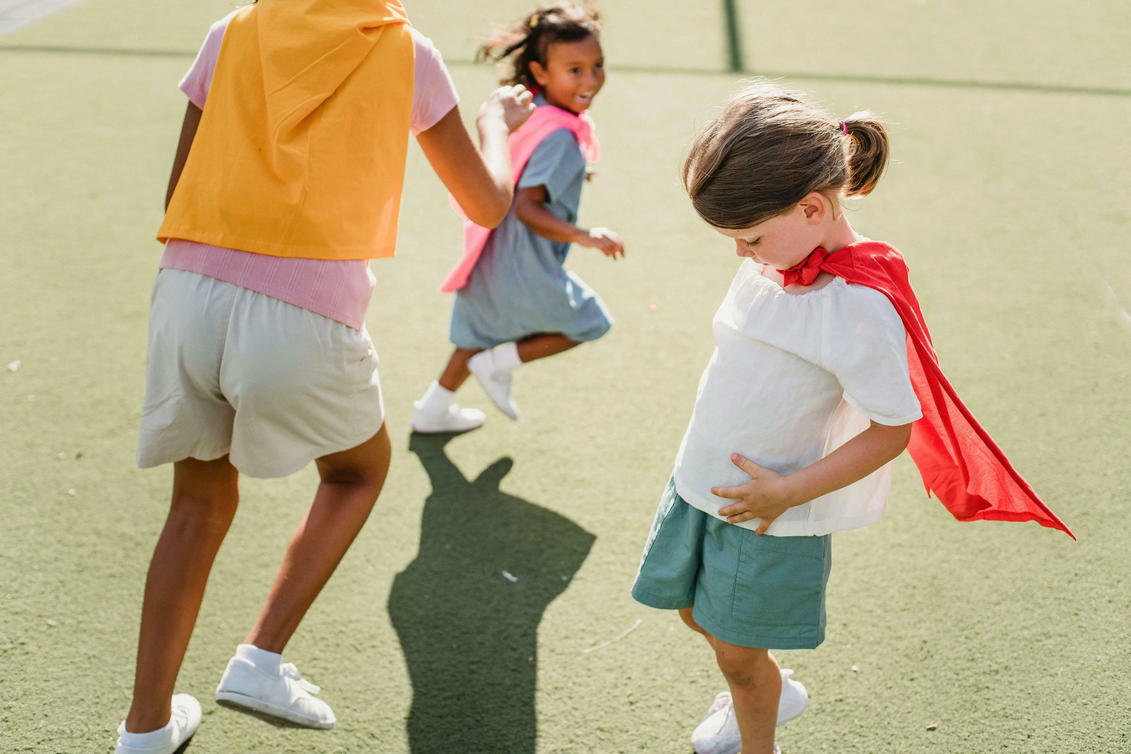 Three young children dressed in capes playing outdoors. A British vocabulary quiz might discuss noughts and crosses.