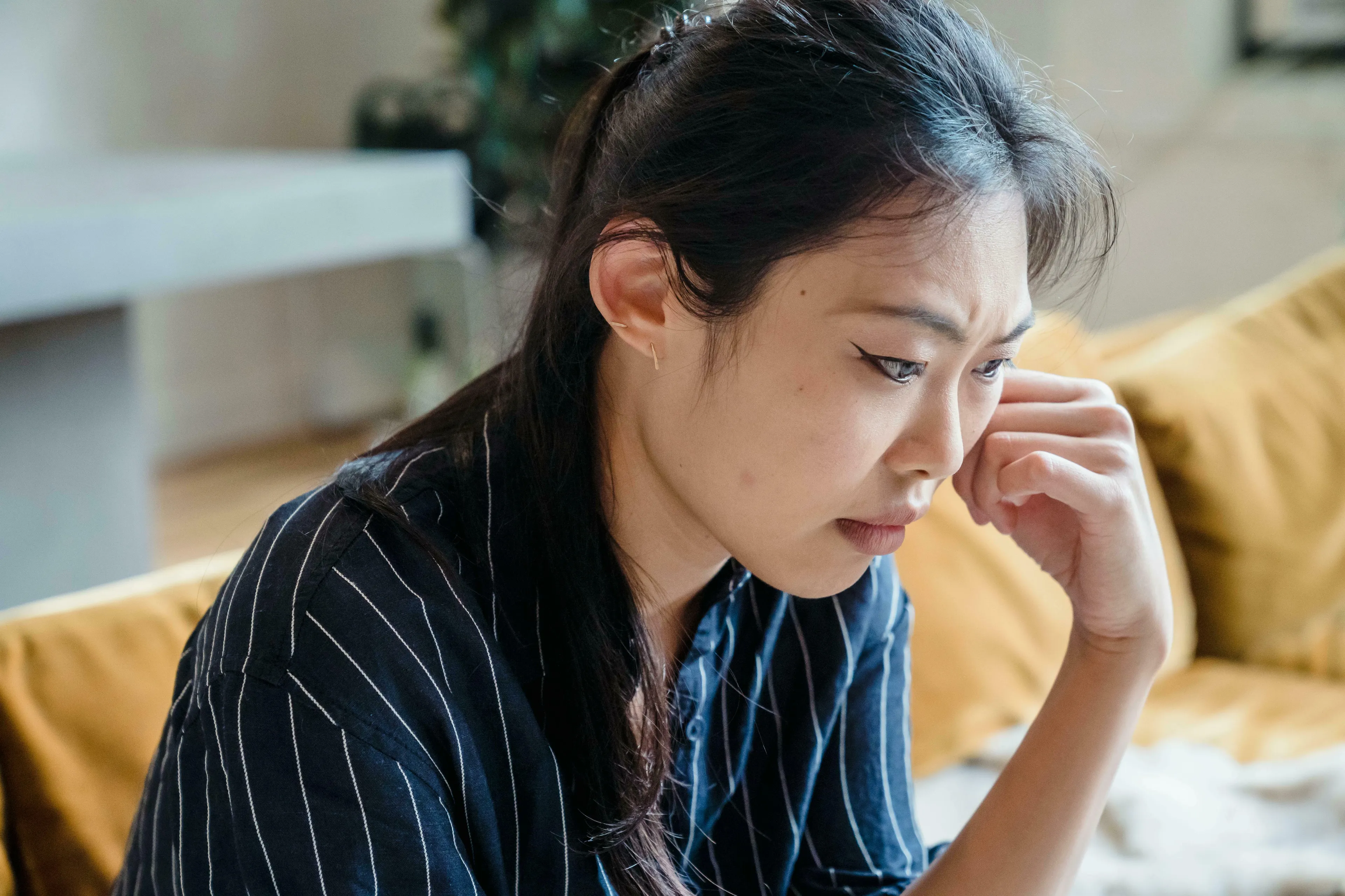 Woman looking down, hand on her face, appearing tired. British Vocabulary Quiz, feeling knackered.