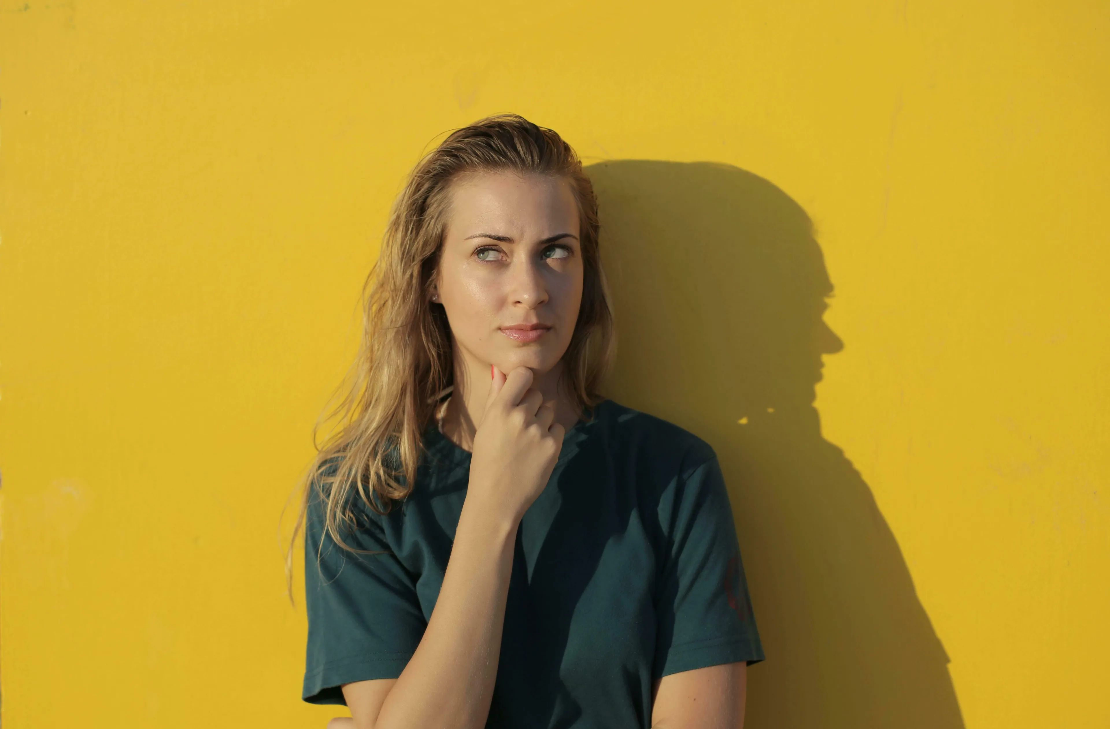 A young woman with blonde hair, deep in thought, on a yellow background. British Vocabulary Quiz.