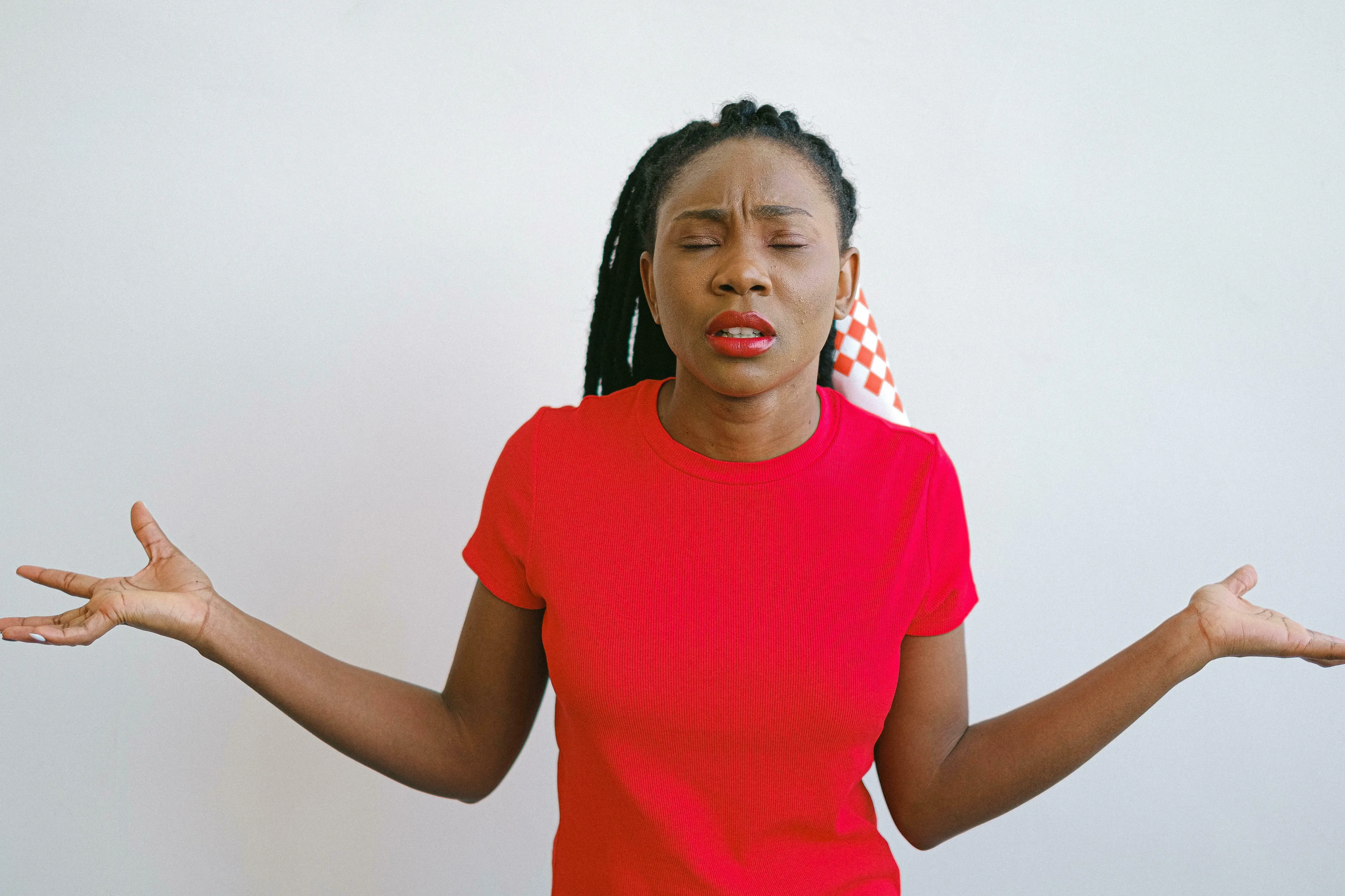 Woman in red t-shirt with braided hair looks confused, hands open in questioning gesture. Exploring British vocabulary and phrases.