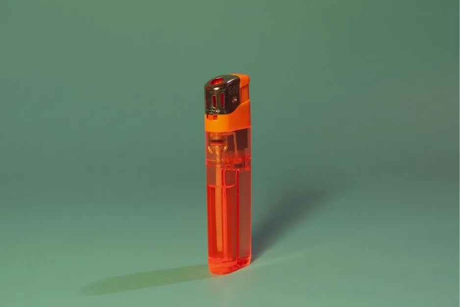 An orange transparent lighter stands upright on a teal background, casting a subtle shadow. A clean, clear shot of a lighter.
