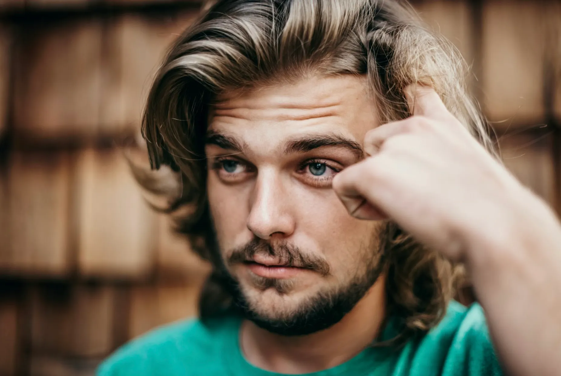 Young man with tousled hair and a thoughtful expression, scratching his temple, perhaps pondering British vocabulary.