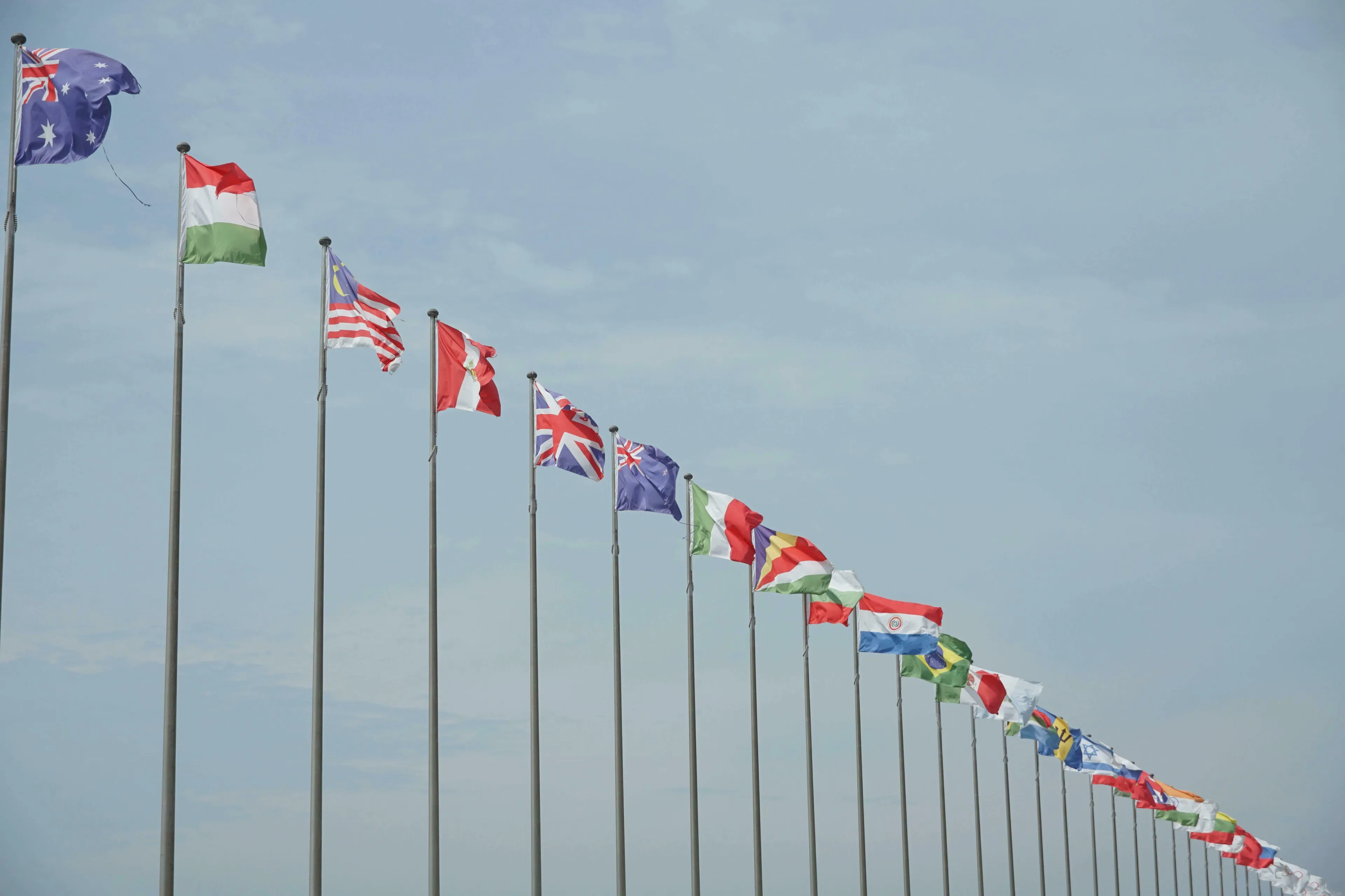 A row of many national flags from various sovereign states, flying against a partly cloudy sky, testing general knowledge.
