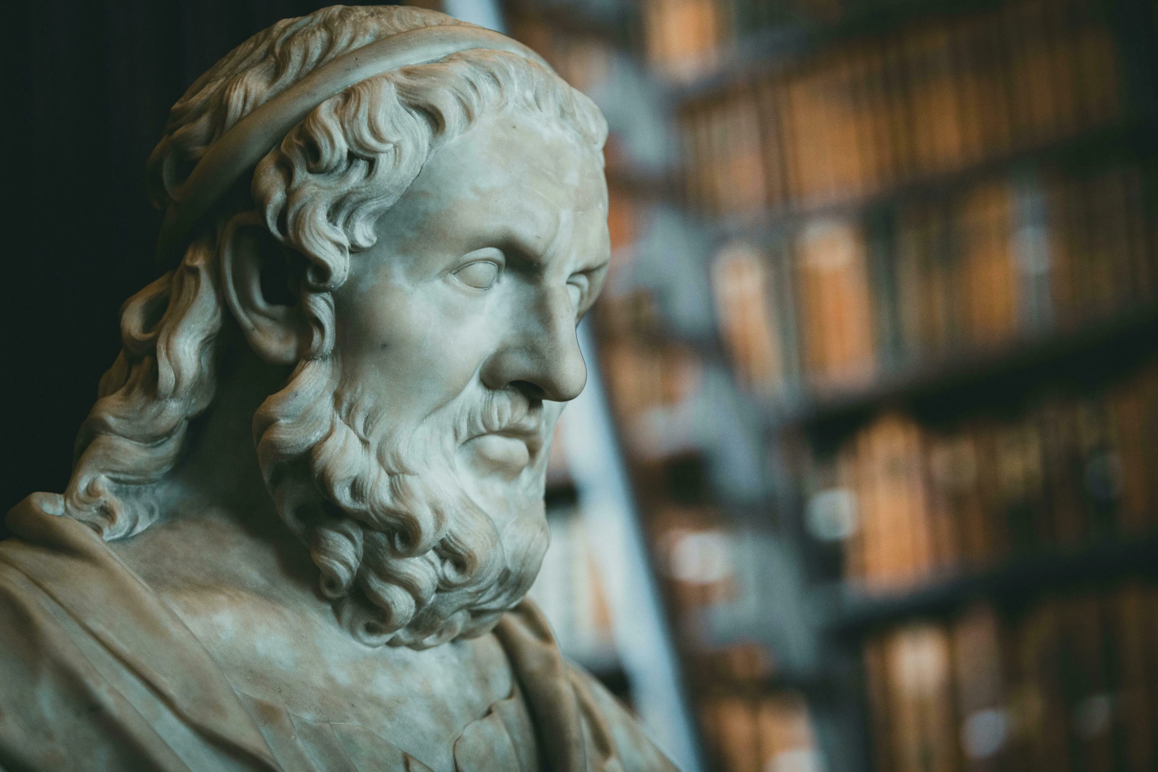 Marble bust of a man with a beard and head wrap, blurred bookshelves behind. General Knowledge Quiz for high IQs.