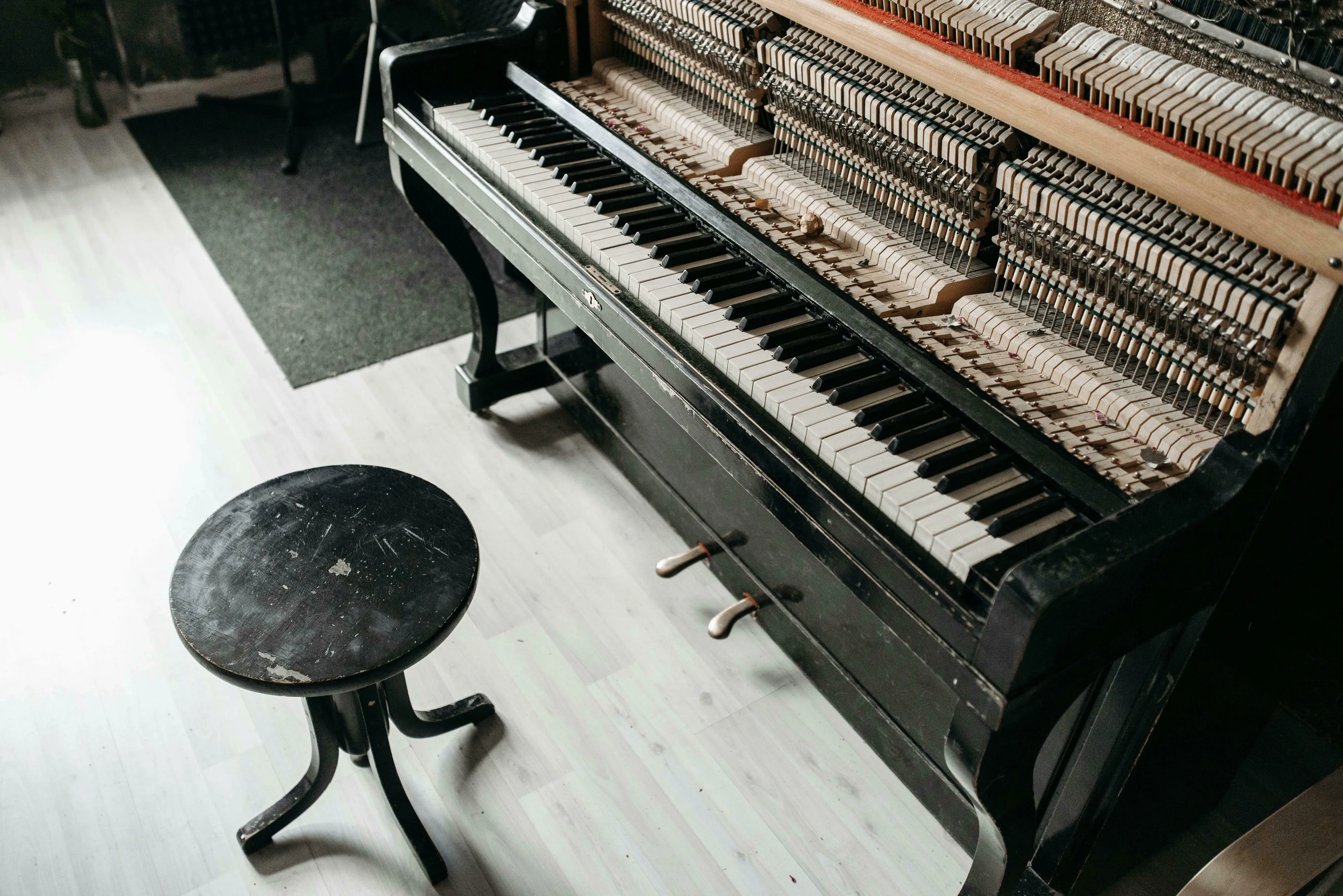 An antique black piano with exposed internal hammers and keys next to a worn black stool. A General Knowledge Quiz awaits.