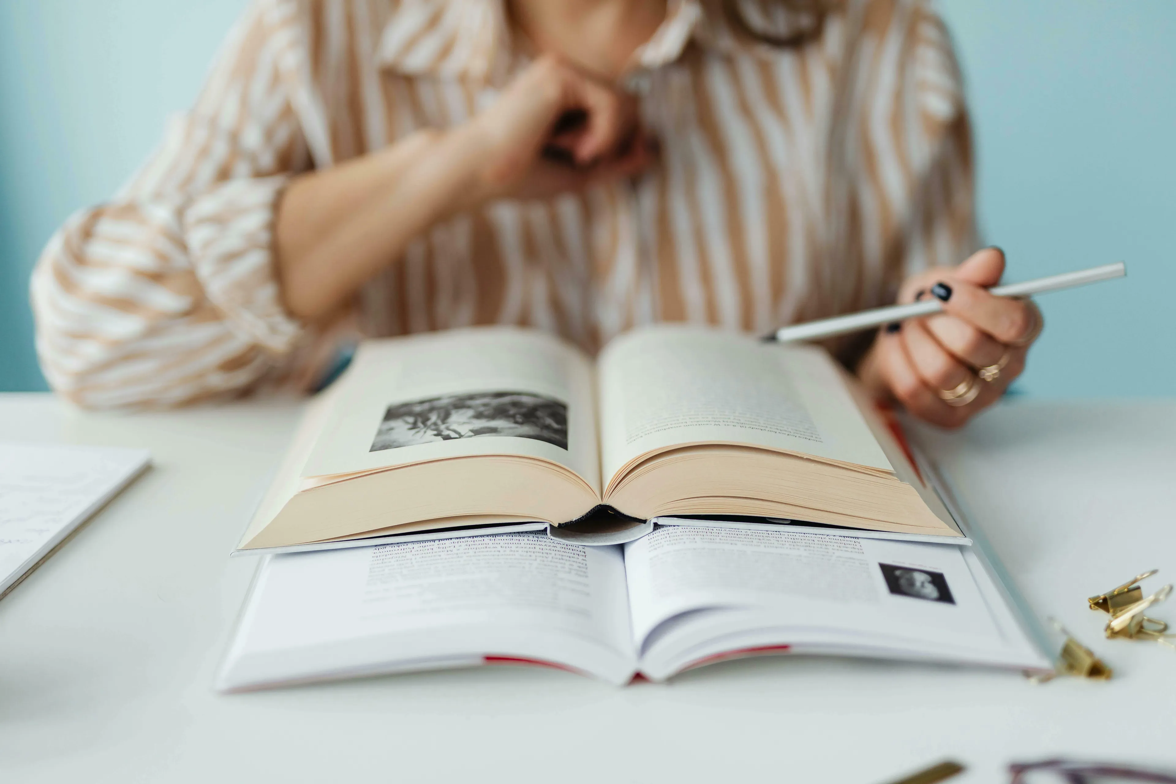 Person reading two open books, holding a pen. Exploring general knowledge for high IQ quizzes about anagrams and acronyms.
