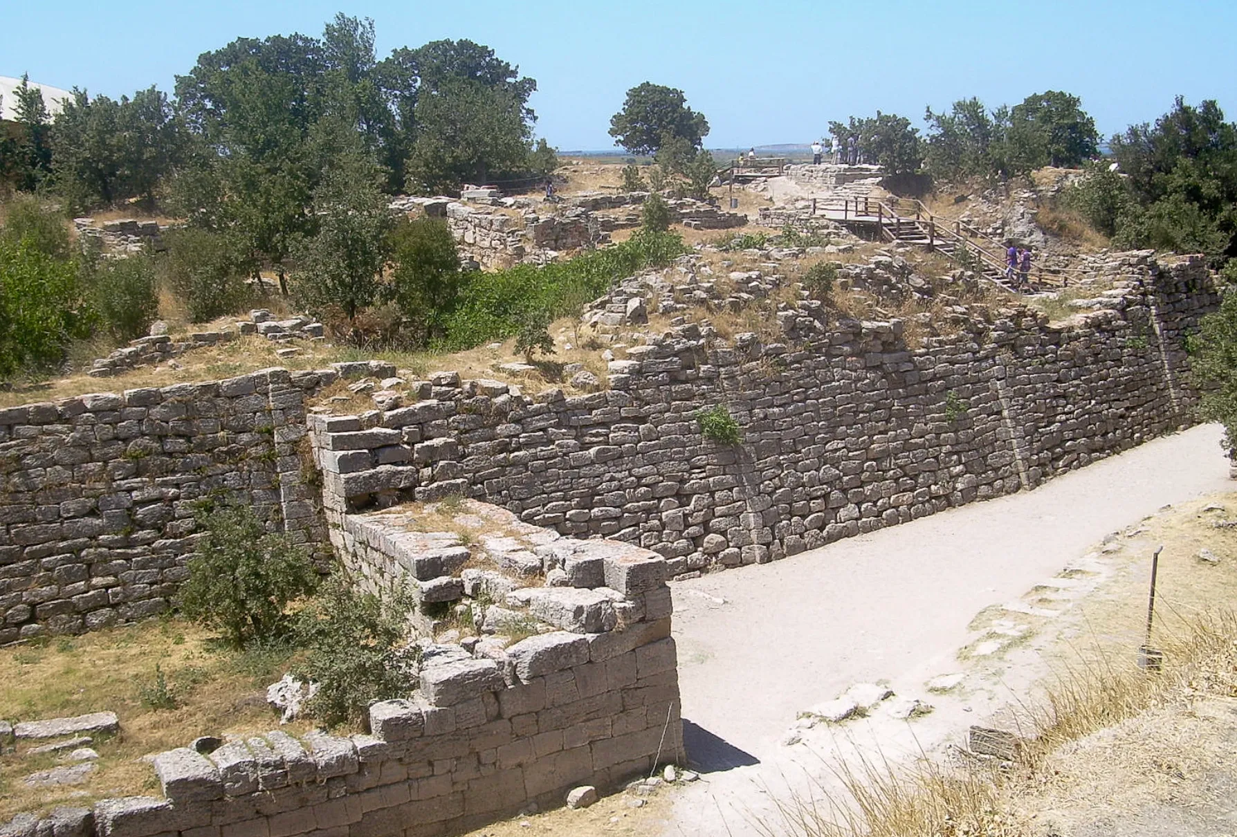 Ancient city of Troy ruins, with weathered stone walls and sparse trees under a blue sky. General Knowledge quiz for high IQs.