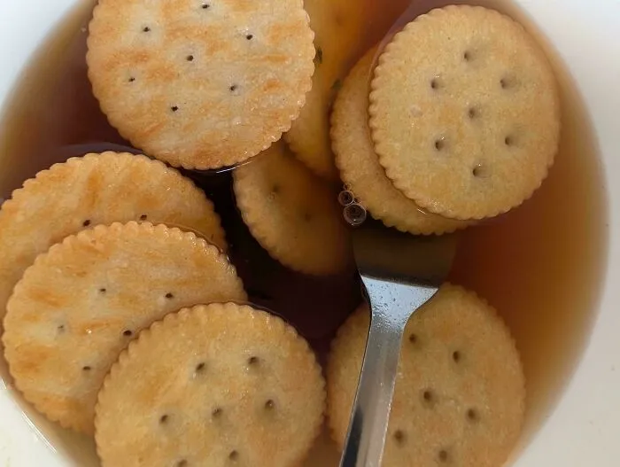 Round salty crackers floating in a bowl of dark tea as a questionable food combo