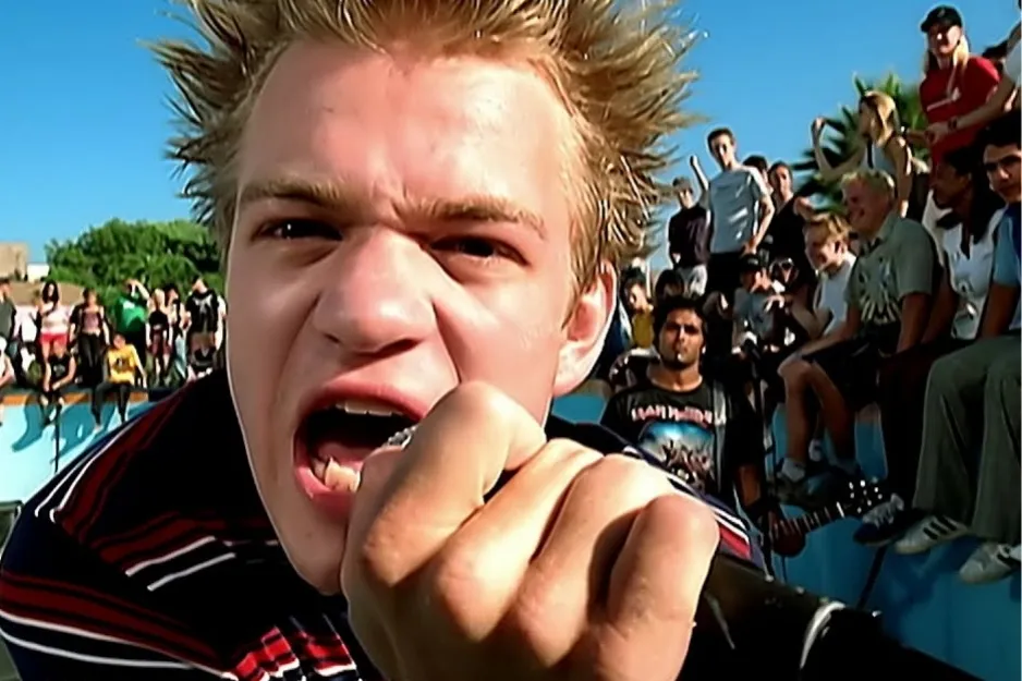 Close-up of a young male singer with spiky hair, microphone in hand, yelling during a Sum 41 performance.