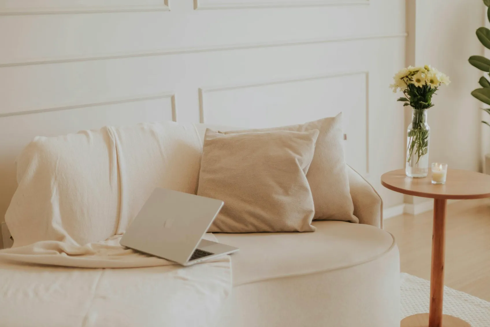 Warm earth tones and linen textures in a cozy living room, featuring a sofa with a laptop, and a side table with flowers.