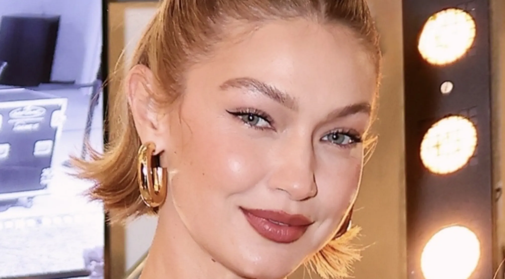 Close-up of a smiling celebrity with light hair, striking eyeliner, and gold hoop earrings. Spell celebrity names.