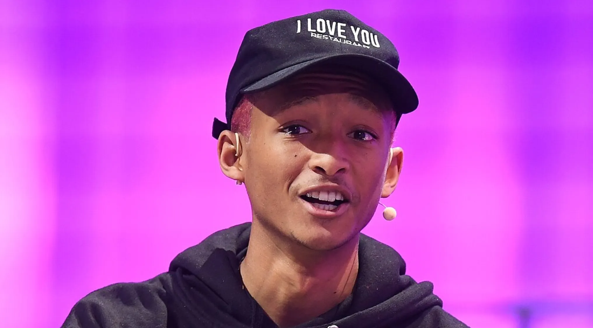 Jaden Smith, a young celebrity, wearing a black cap and hoodie, speaking into a microphone. What is this person's name?