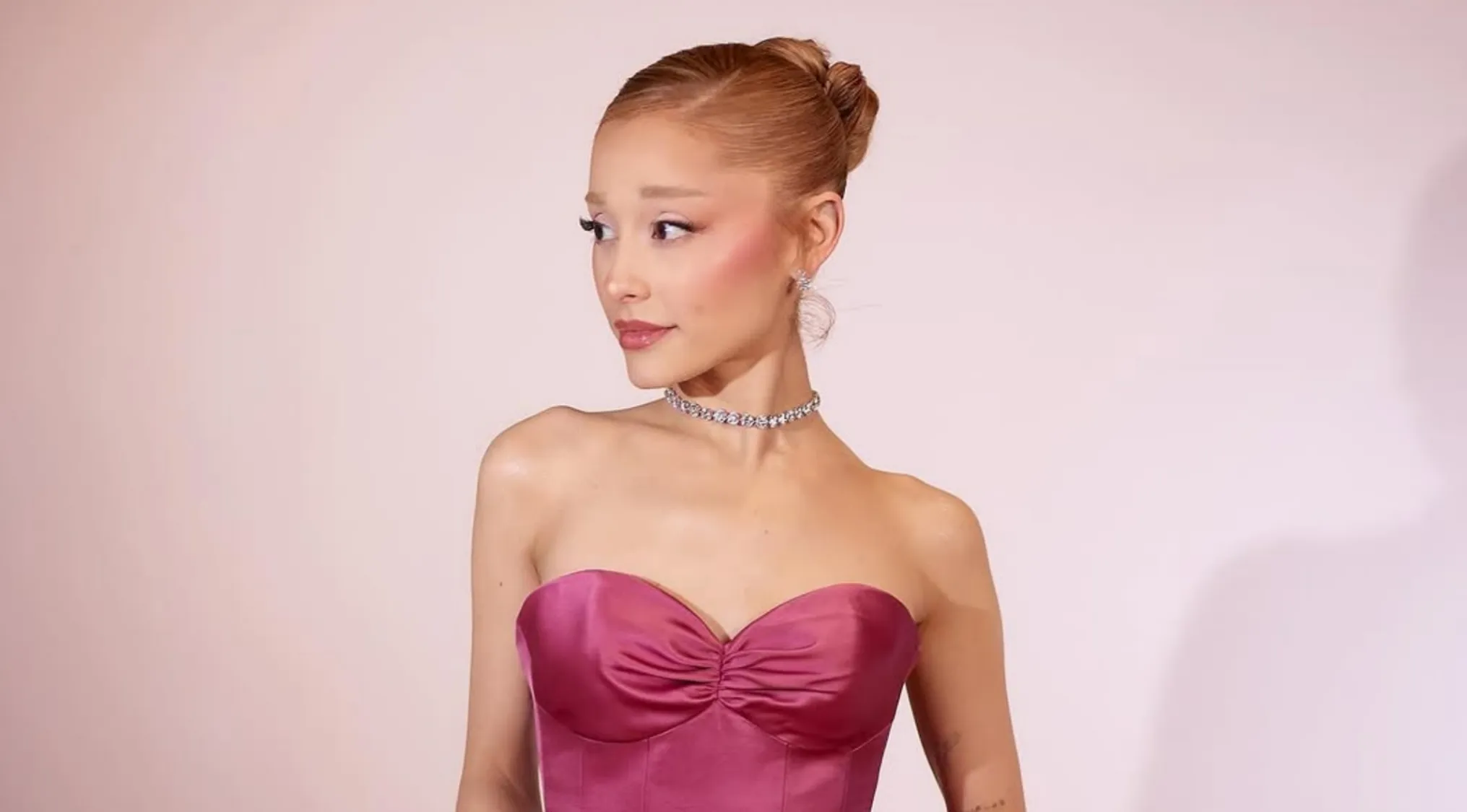 Ariana Grande poses in a pink dress, diamond choker and earrings, contemplating Real Or Fake Trivia about her Taekwondo skills.