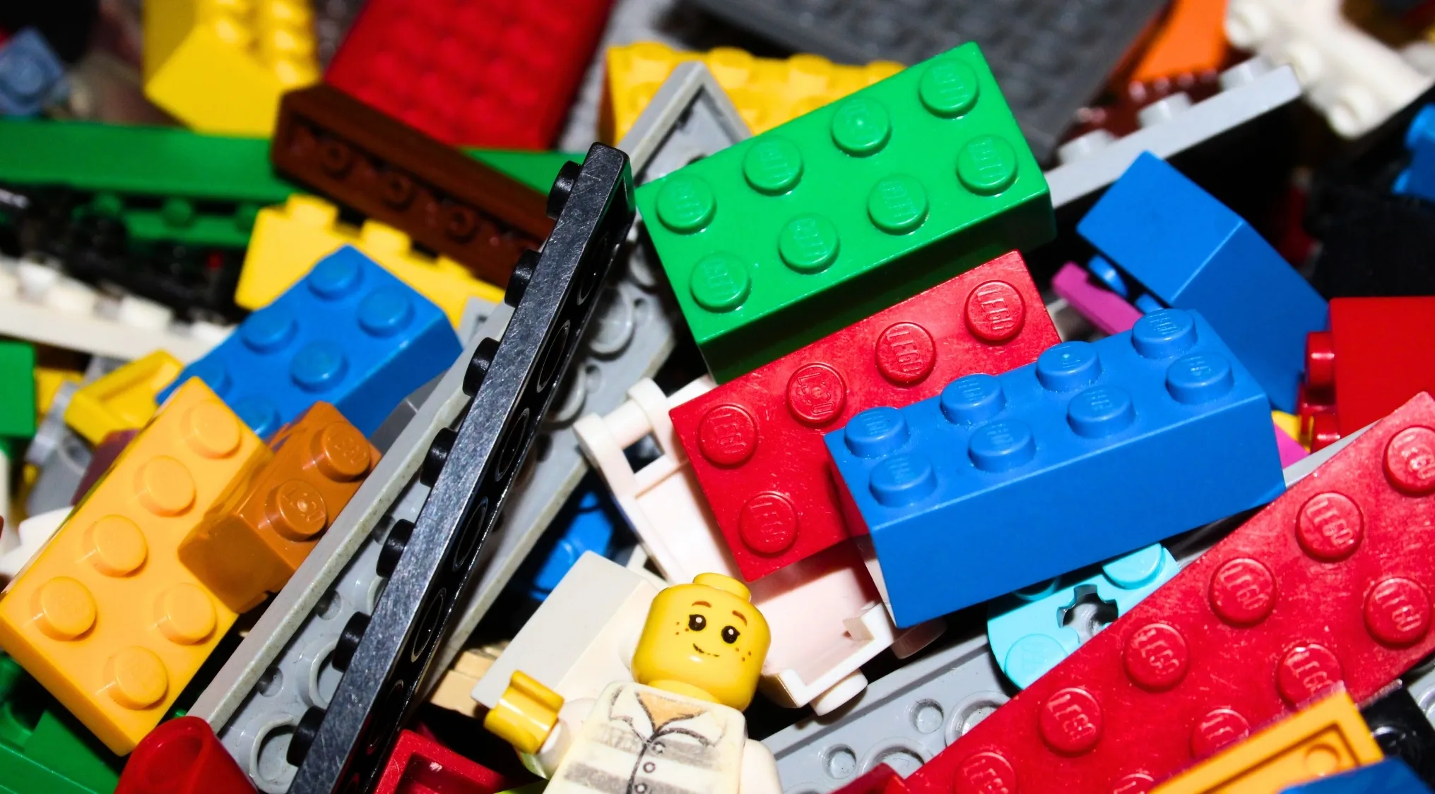 A pile of colorful LEGO bricks and a smiling LEGO minifigure, perfect for genuine LEGO brick trivia.