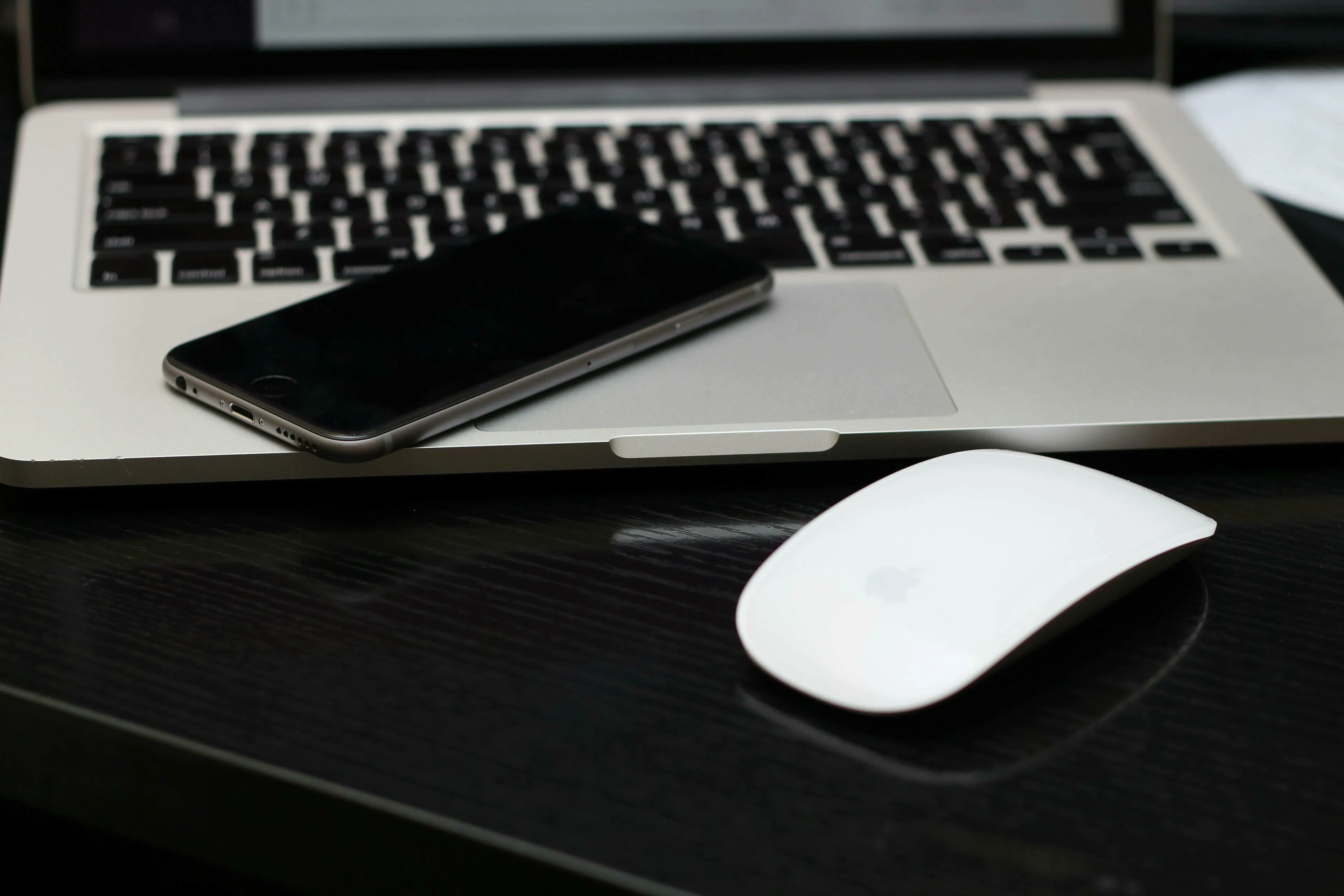 A white computer mouse, an iPhone, and a laptop keyboard on a dark desk. Real or fake trivia.