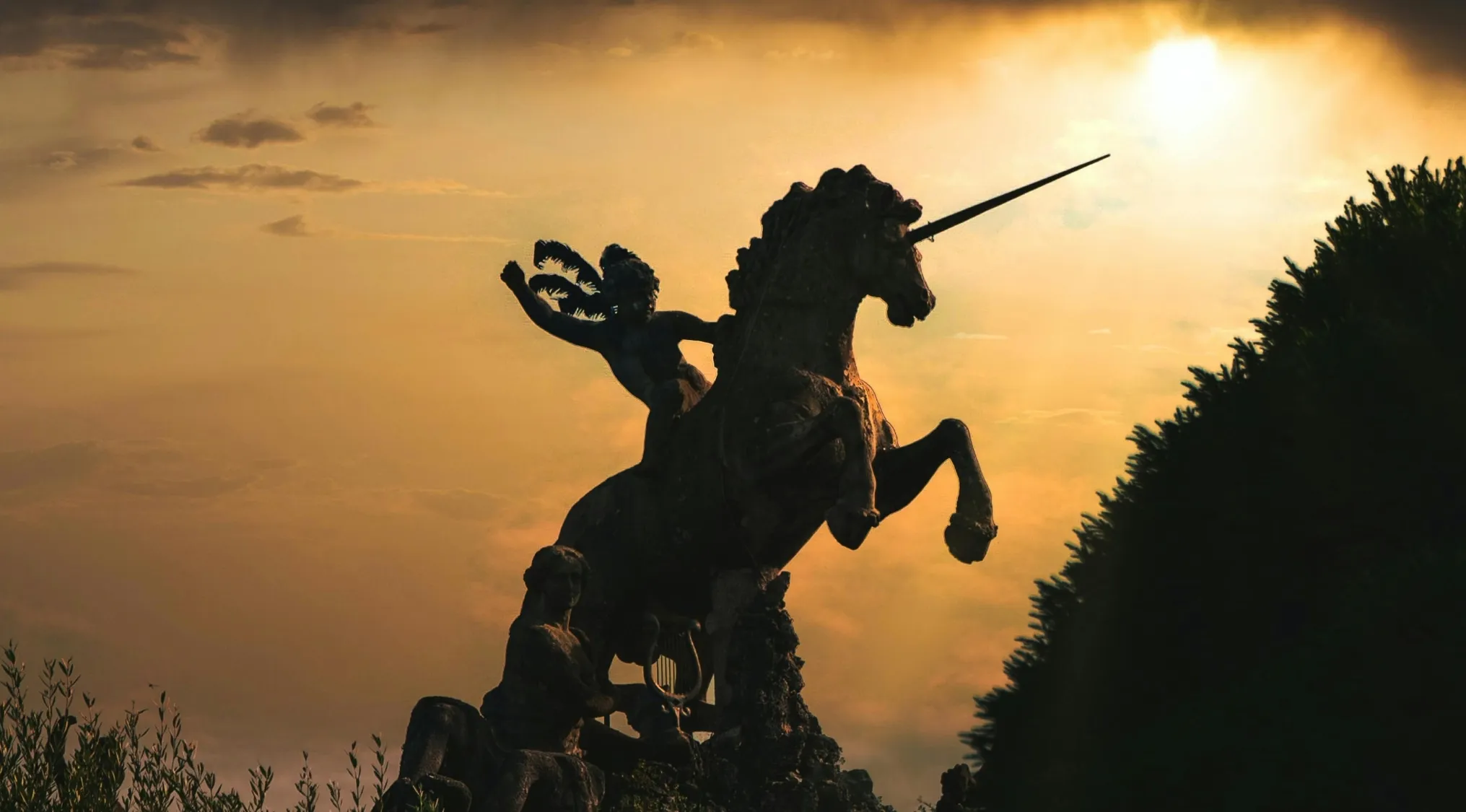 A dark silhouette of a statue showing a figure riding a unicorn, back-lit by a dramatic sunset. Real or Fake Trivia.