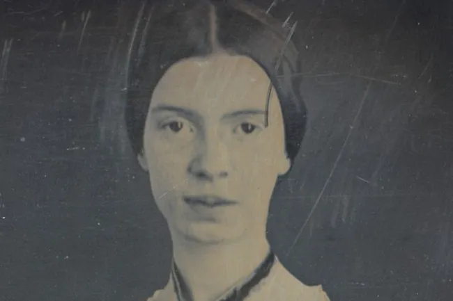 An aged photograph of Emily Dickinson, a historical figure, looking directly at the viewer with a serious expression.