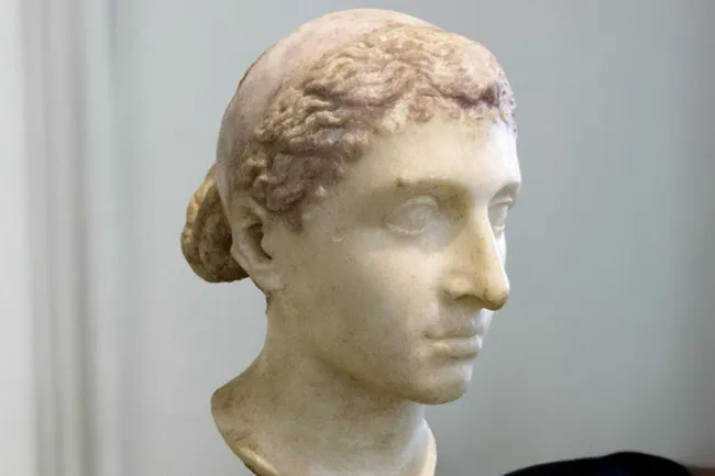 A marble bust of Cleopatra, head turned slightly right, with intricately carved hair tied back.