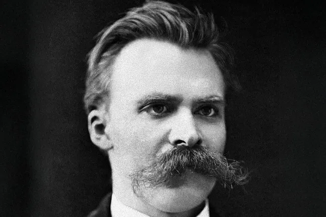 Black and white portrait of Friedrich Nietzsche, with a prominent mustache, looking intensely forward.