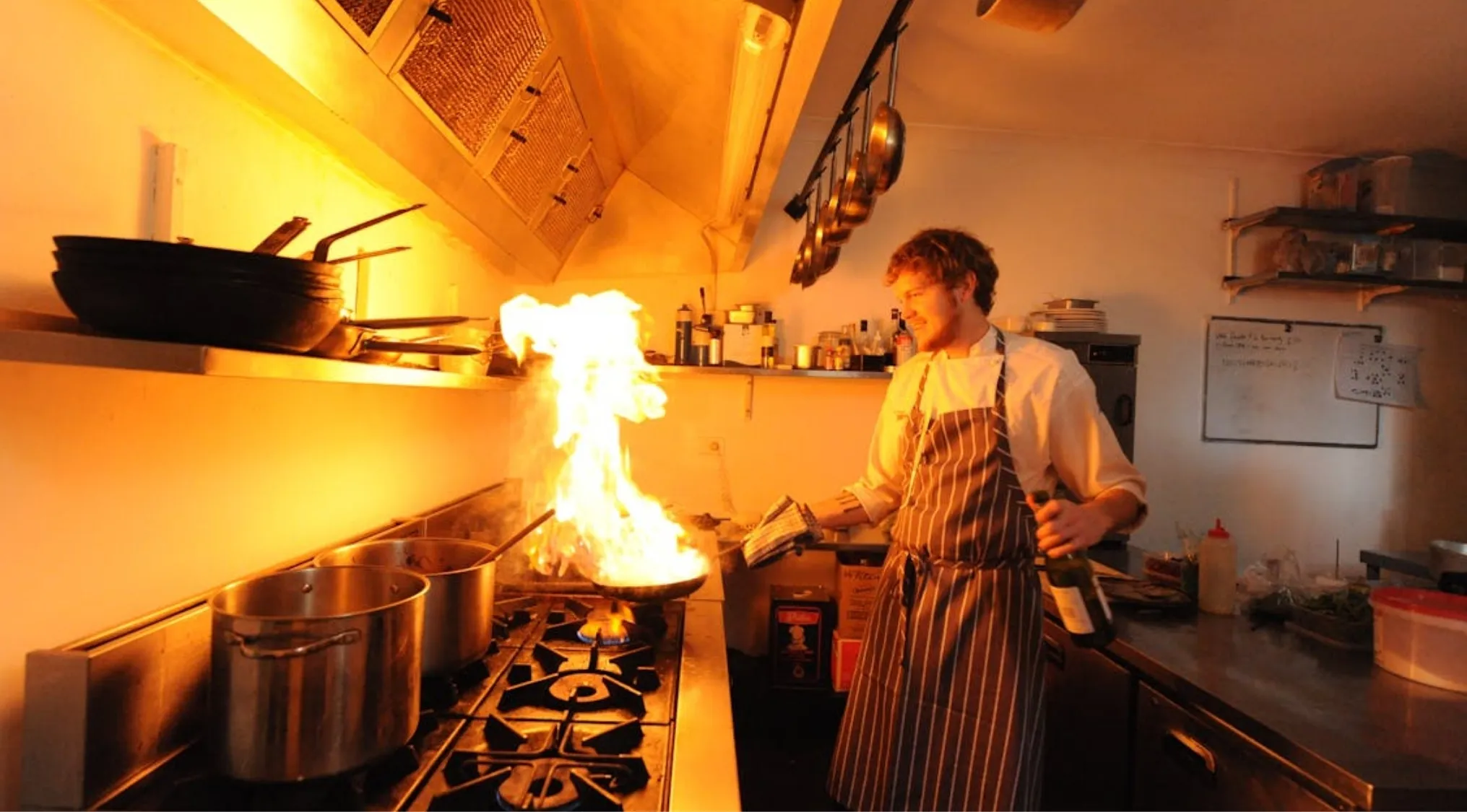 A smiling chef with a grease fire in the kitchen, cooking on a gas stove. Home Economics safety tips.