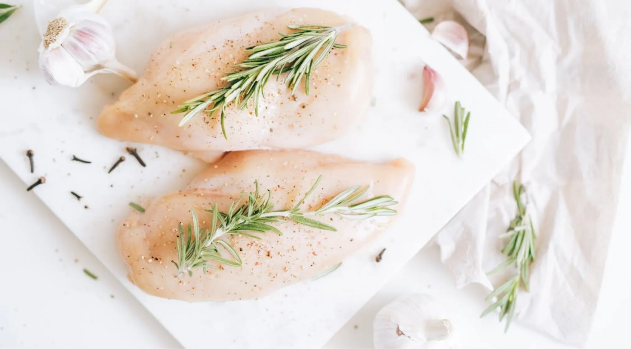 Home Economics: Two raw chicken breasts seasoned with rosemary and pepper, ready for cooking to proper internal temperature.