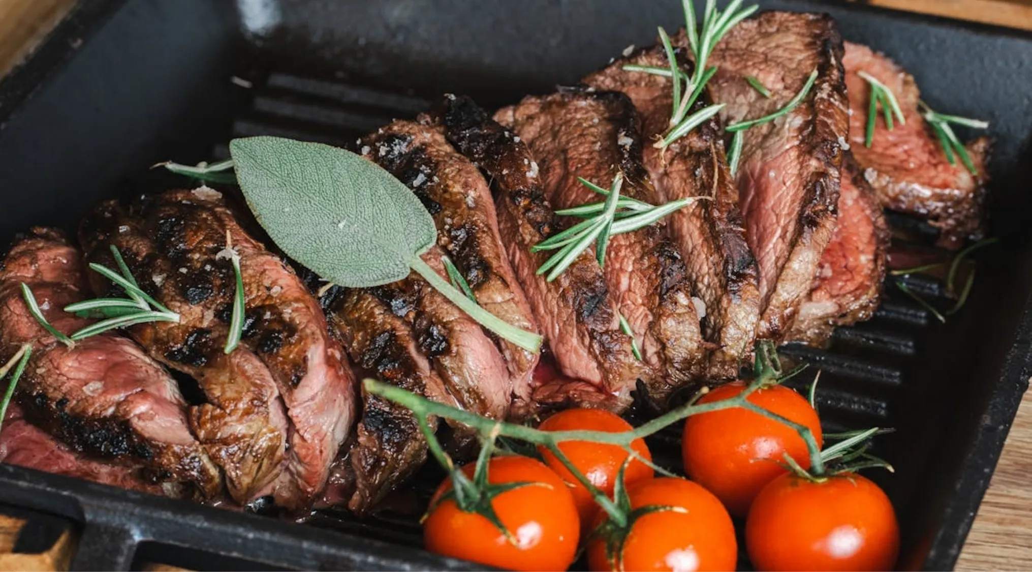 Perfectly cooked meat resting on a grill pan with rosemary, sage, and cherry tomatoes. Let meat rest for best results.