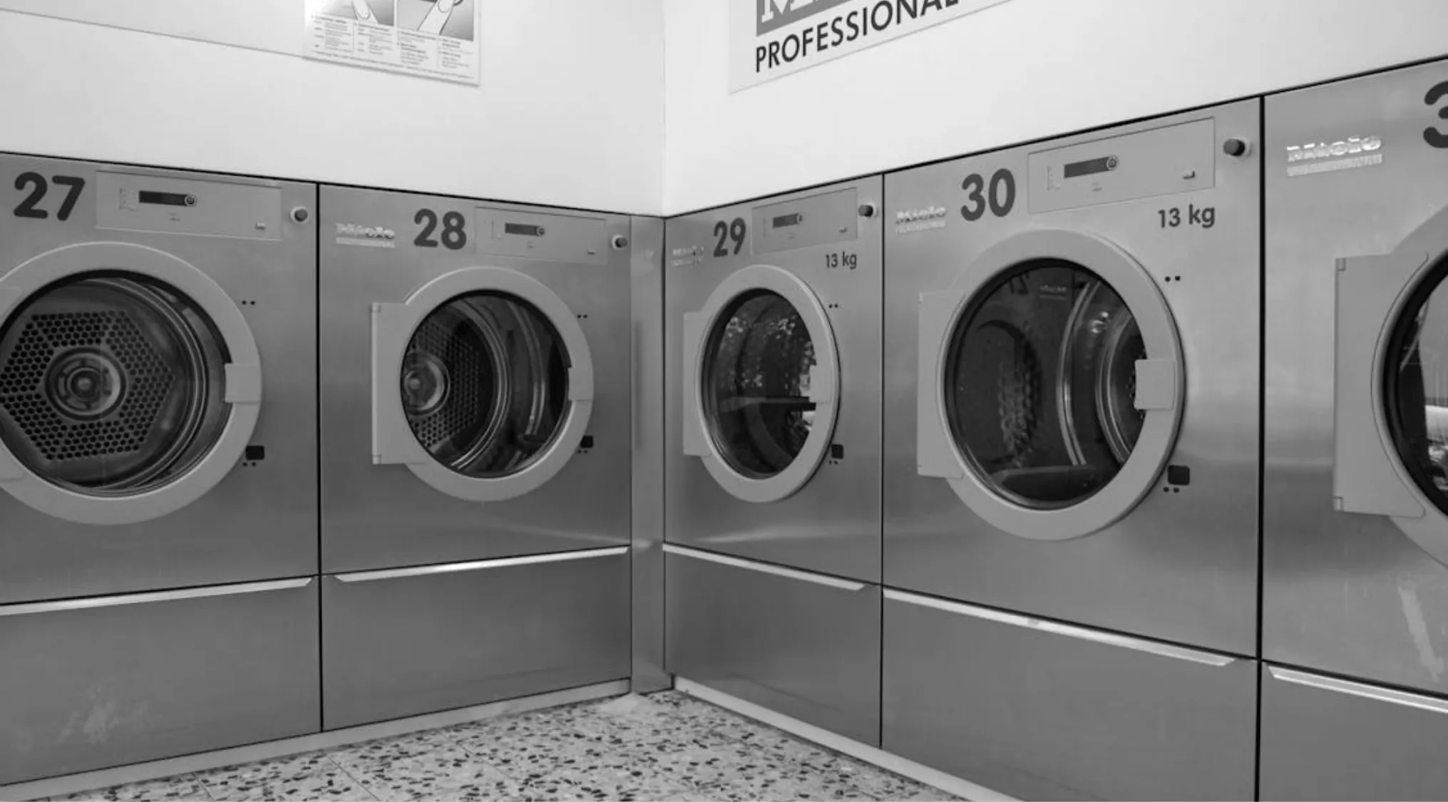 Row of industrial washing machines in a laundromat, relevant to home economics and how often to drain for preventing mold.