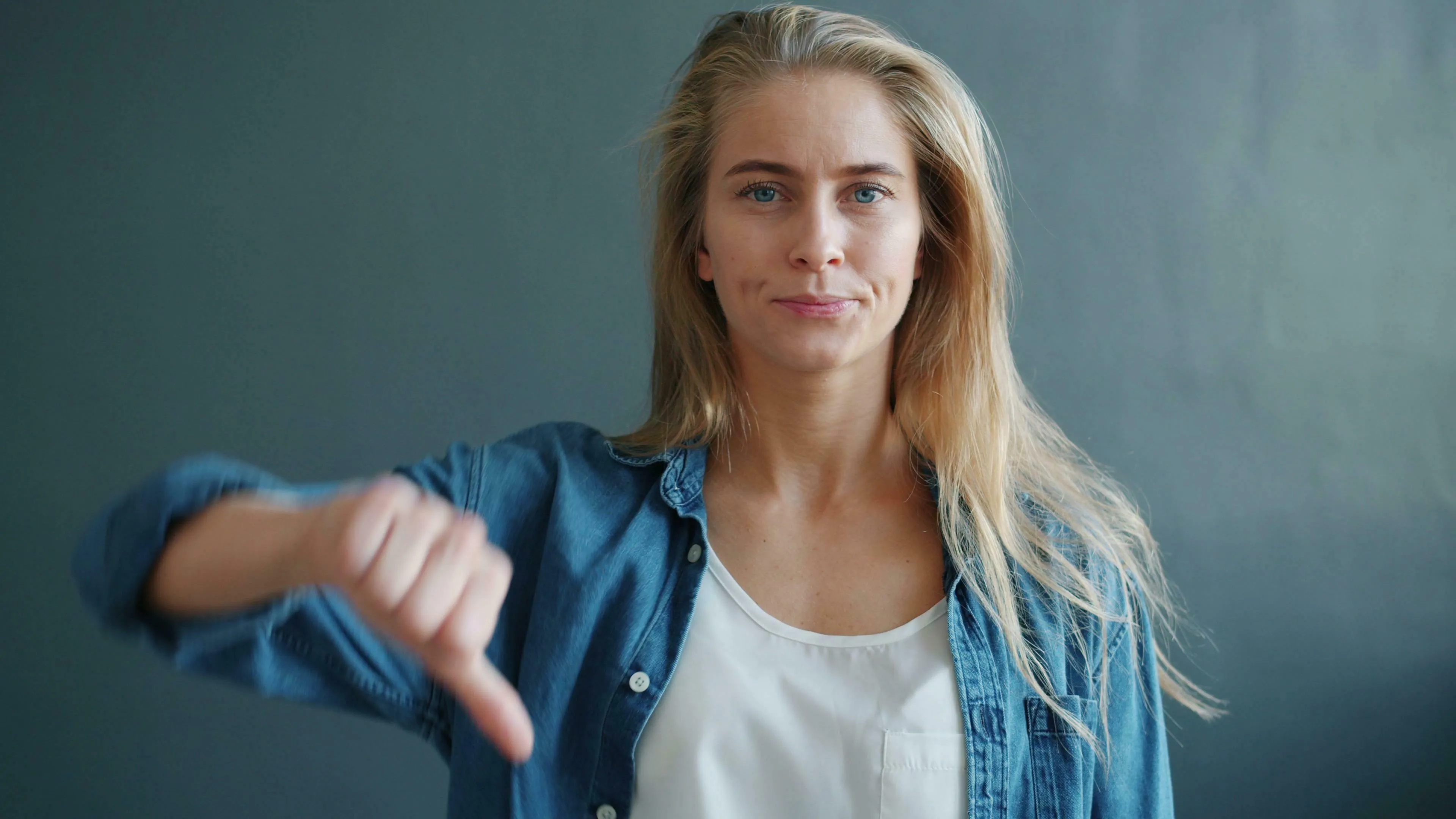 A woman in a denim shirt gives a thumbs-down. She appears unique in her negative opinion.