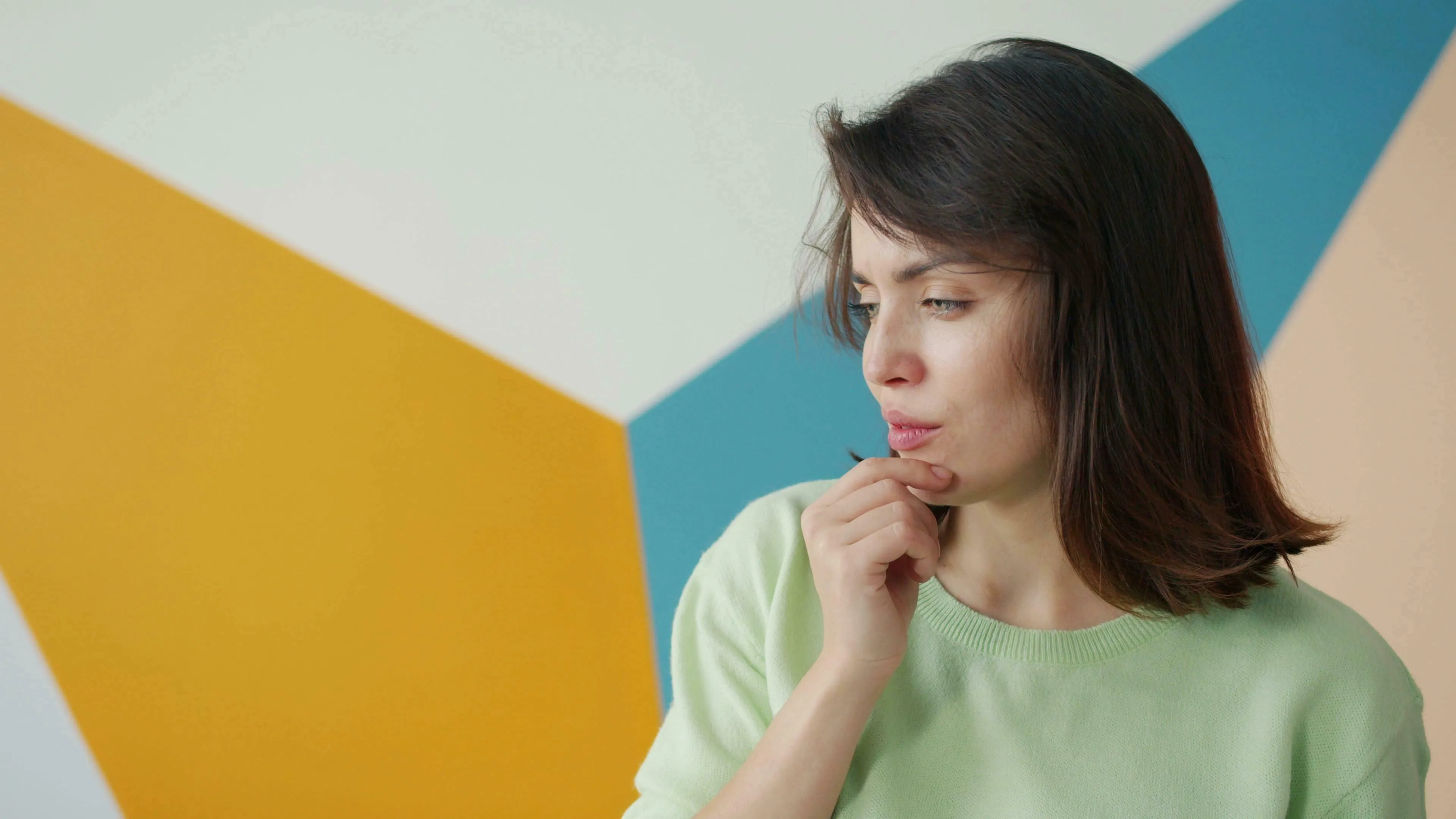 A young woman in a light green sweater looking thoughtfully, touching her chin against a colorful geometric background. How unique are you?