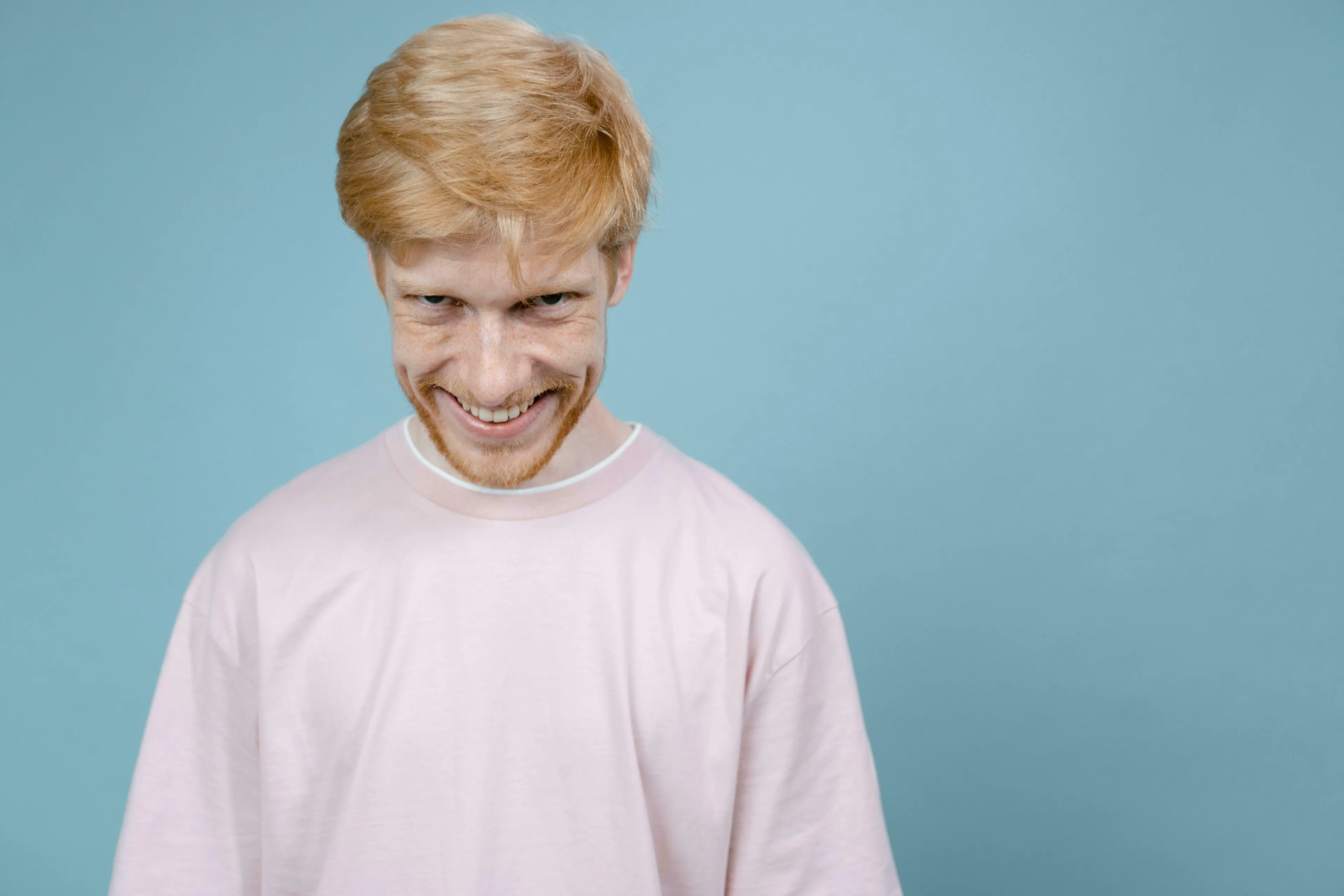A smiling ginger man with freckles and a light pink shirt, hinting at a secretly agreed unpopular opinion.