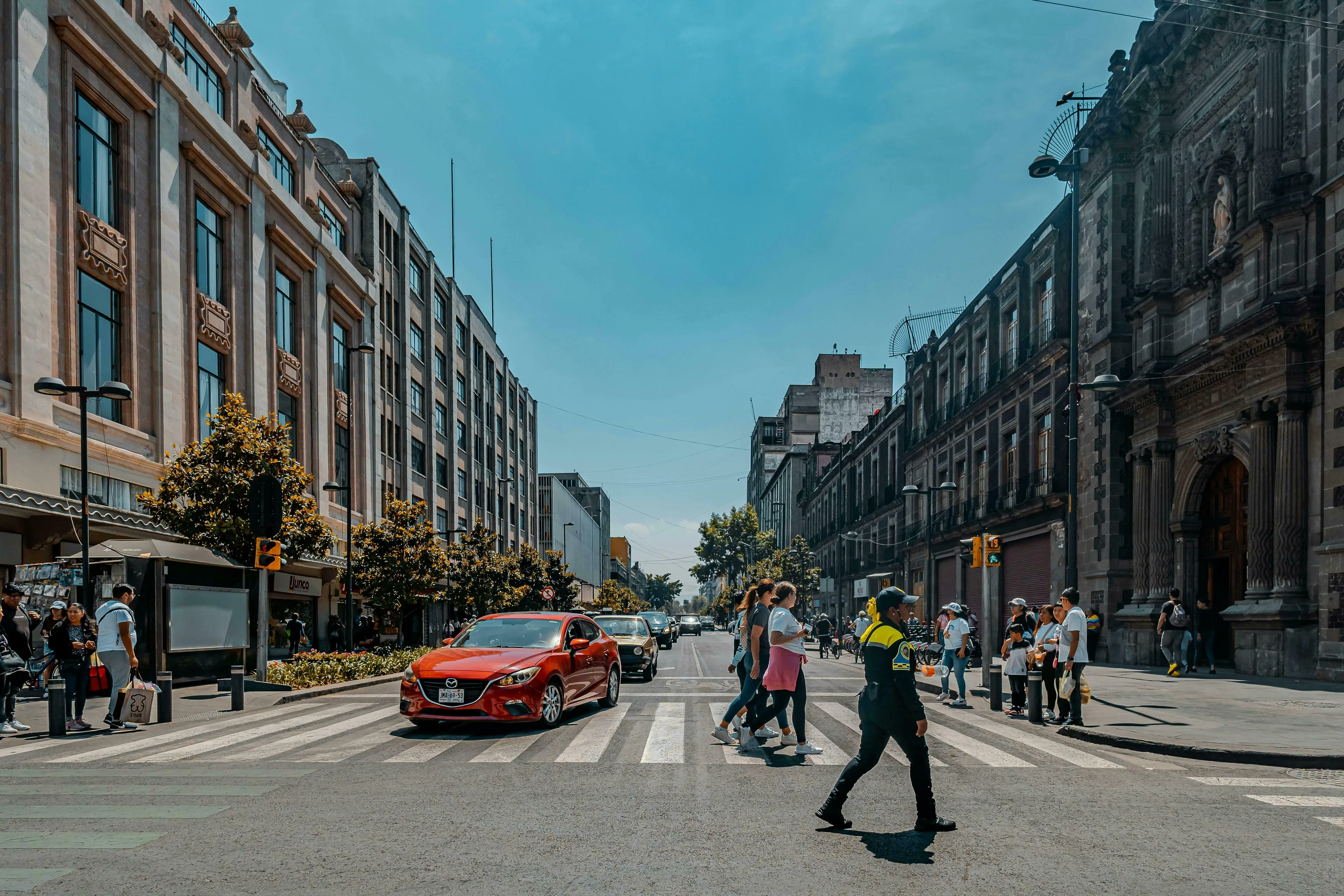 A bustling city street with people crossing the road and cars, on the first day in a new city.