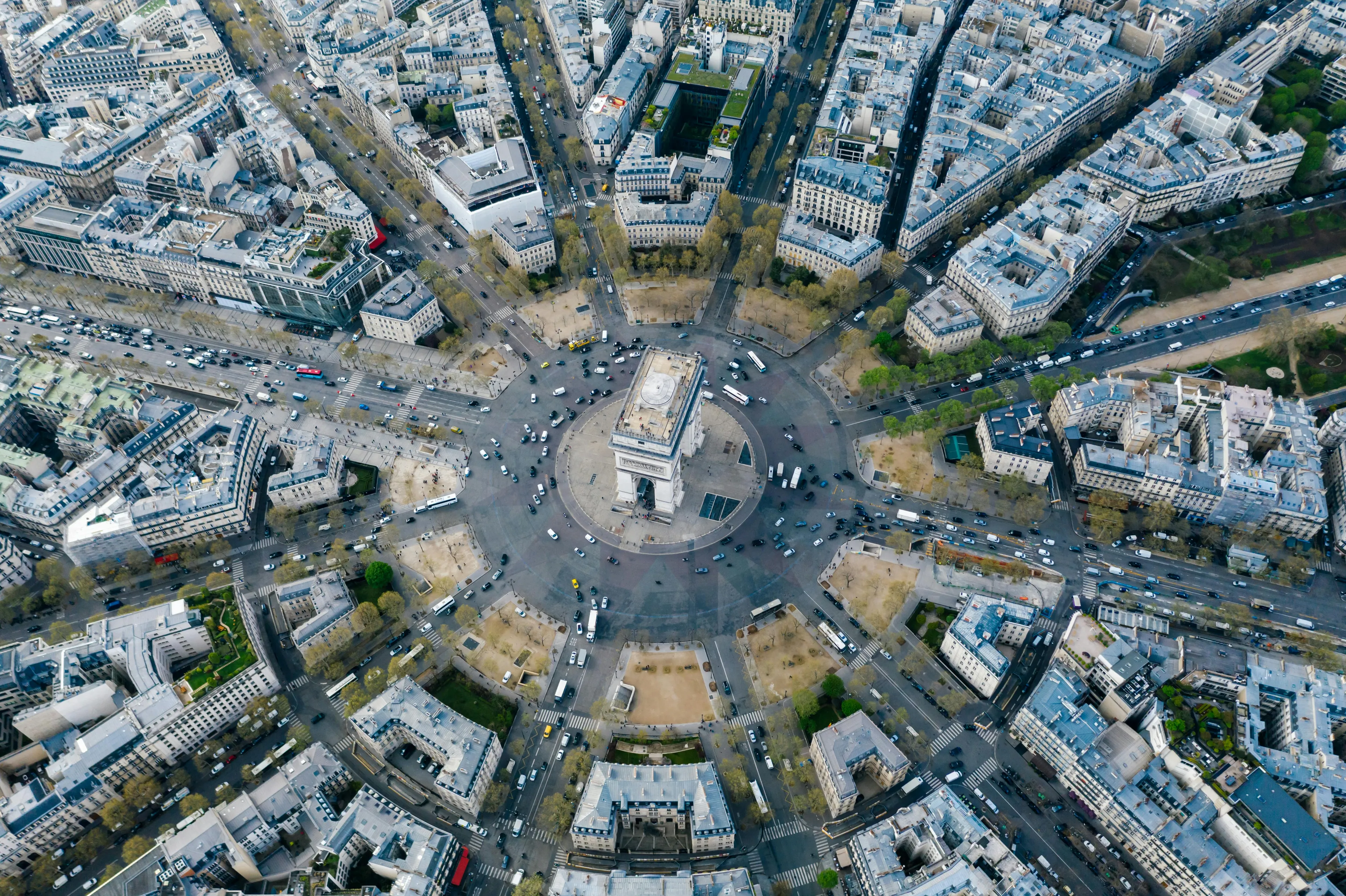 Aerial view of the Arc de Triomphe and surrounding streets in Paris, bustling with cars. A great long weekend destination!