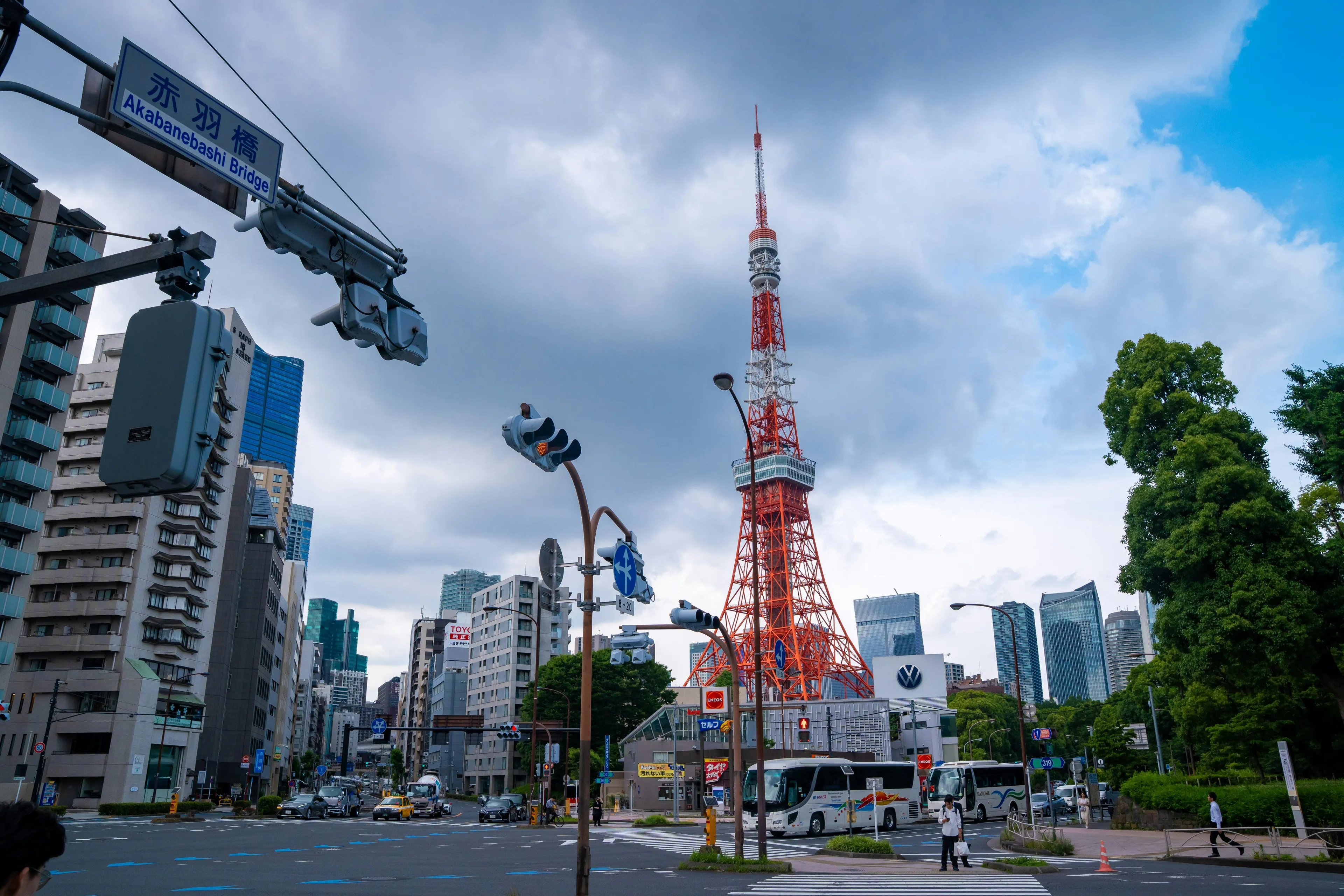 A street view in Tokyo featuring the iconic red and white Tokyo Tower, cars, and buildings under a cloudy sky.