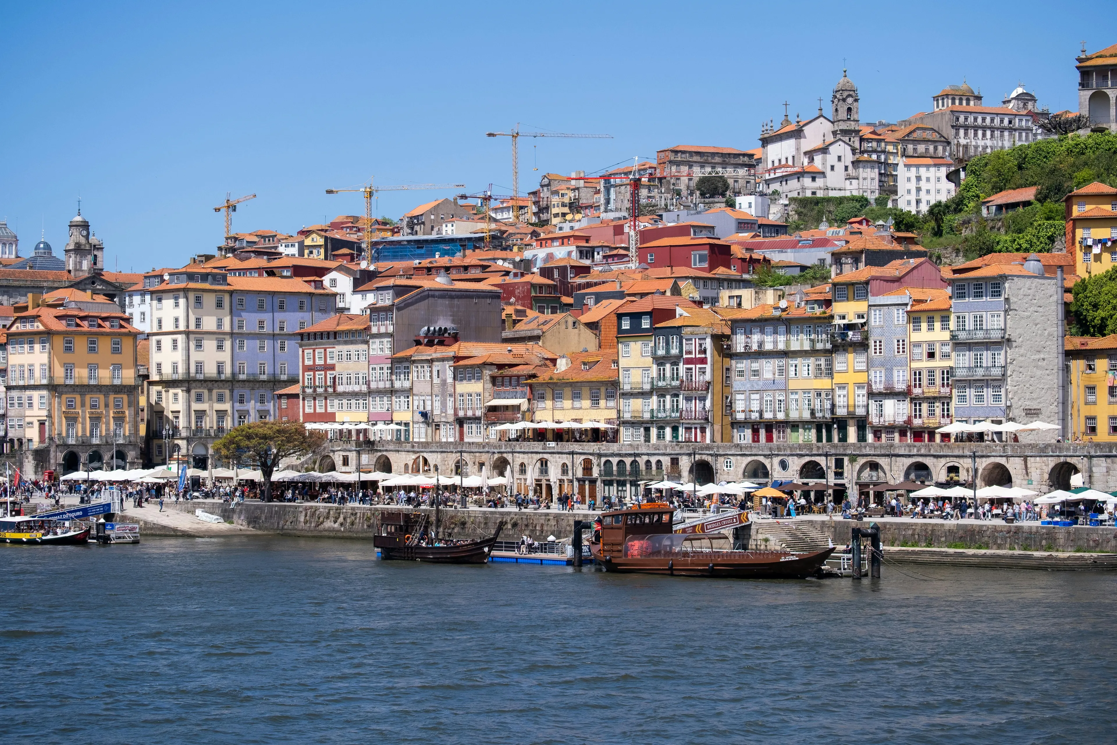 Vibrant Porto cityscape with colorful buildings cascading down to the Douro River, bustling with boats and people enjoying a long weekend.