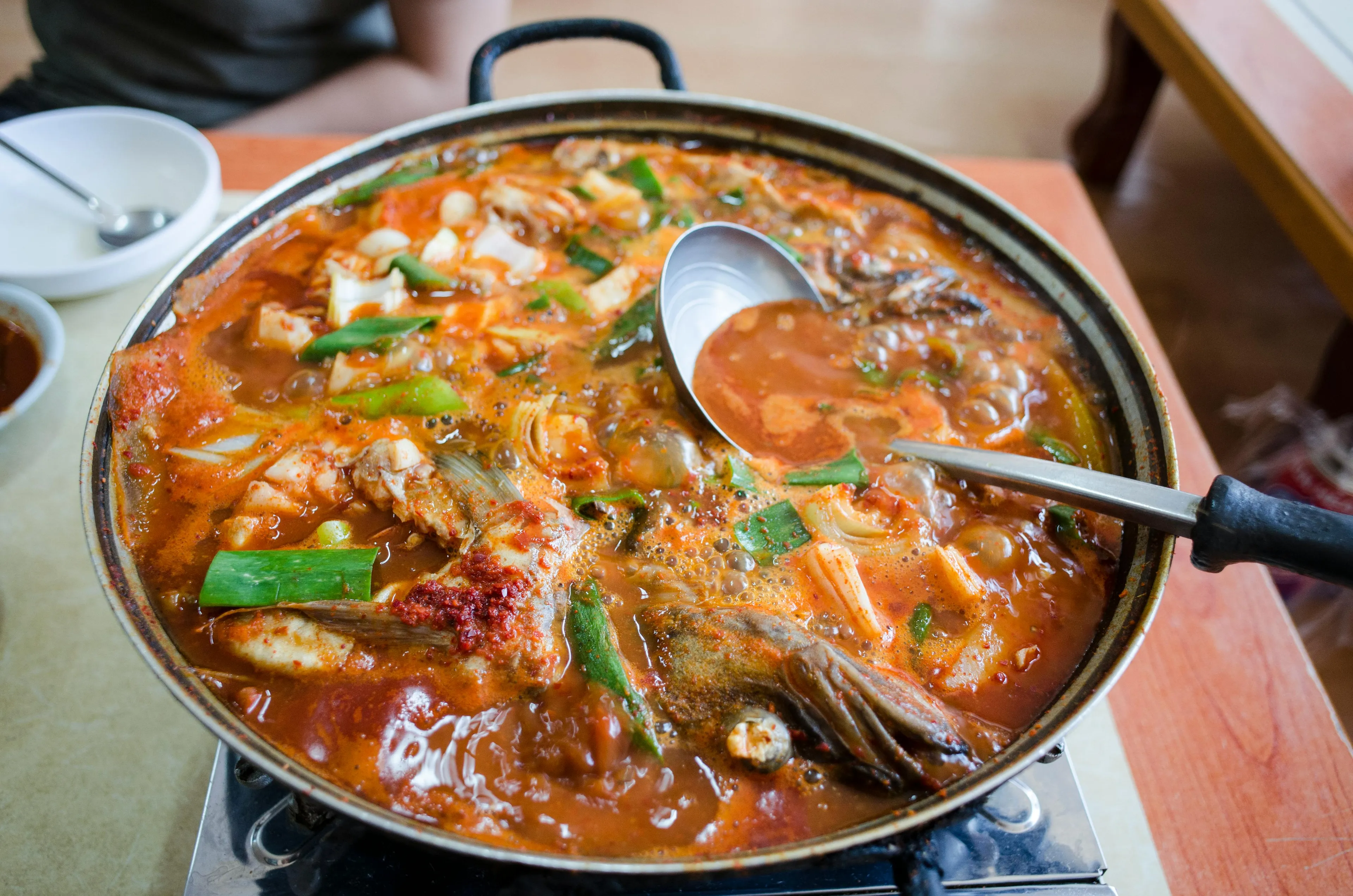 A sizzling pot of vibrant kimchi stew with seafood and vegetables, being stirred with a ladle. A delicious meal.