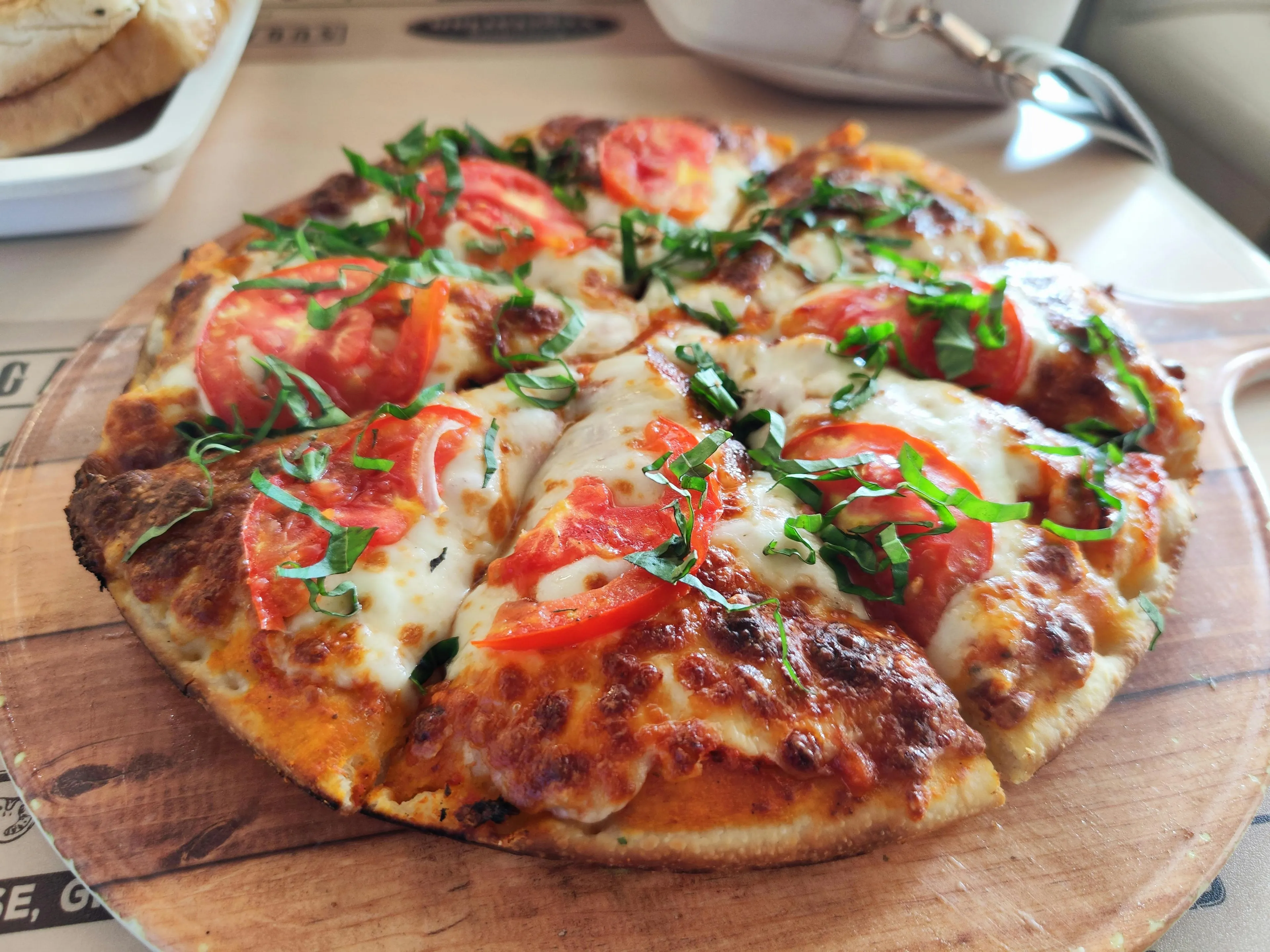 Delicious pizza with sliced tomatoes, melted mozzarella, and fresh basil, served as a perfect meal on a wooden board.