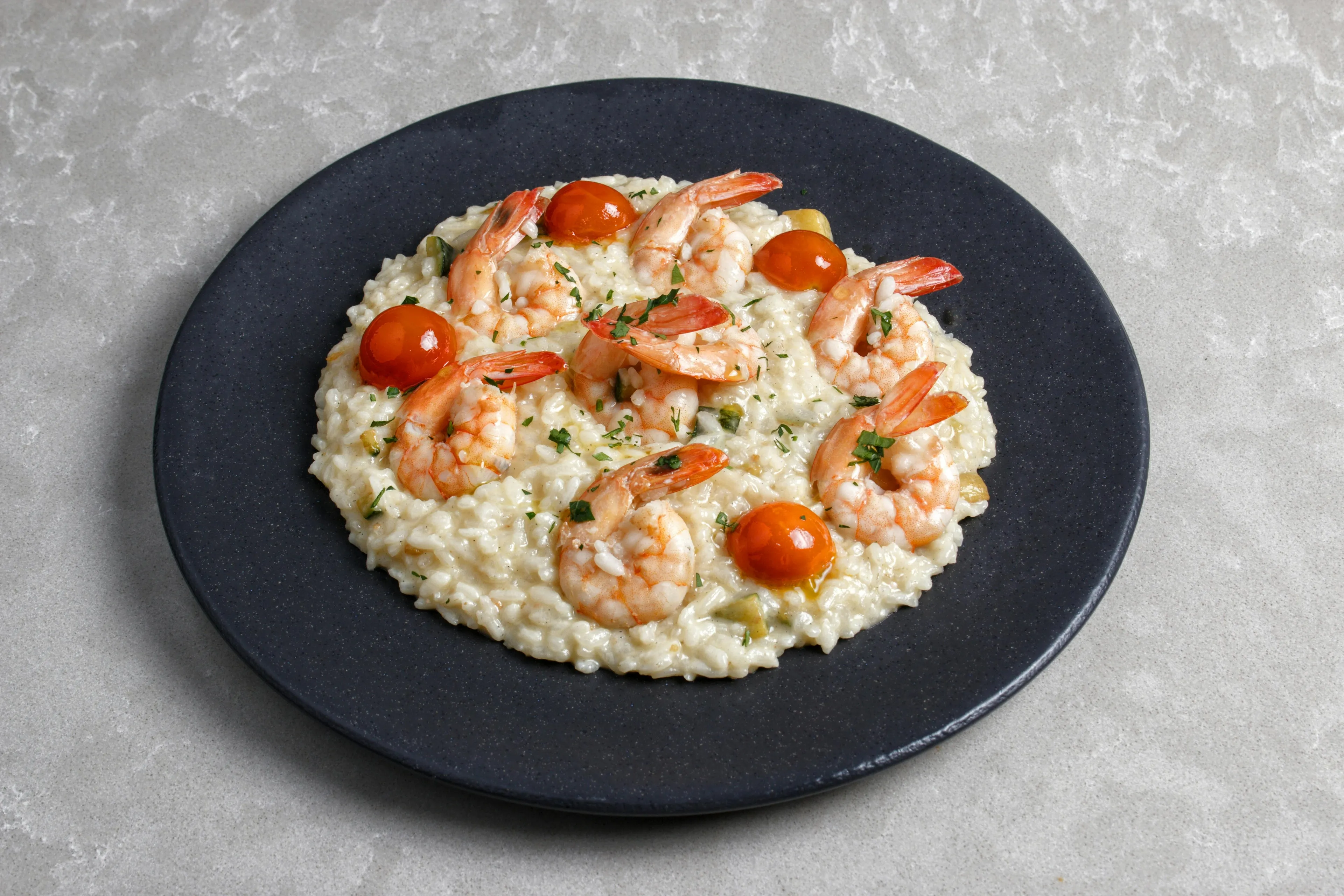 Creamy shrimp risotto topped with cherry tomatoes and fresh herbs, served on a dark plate. A delicious meal.