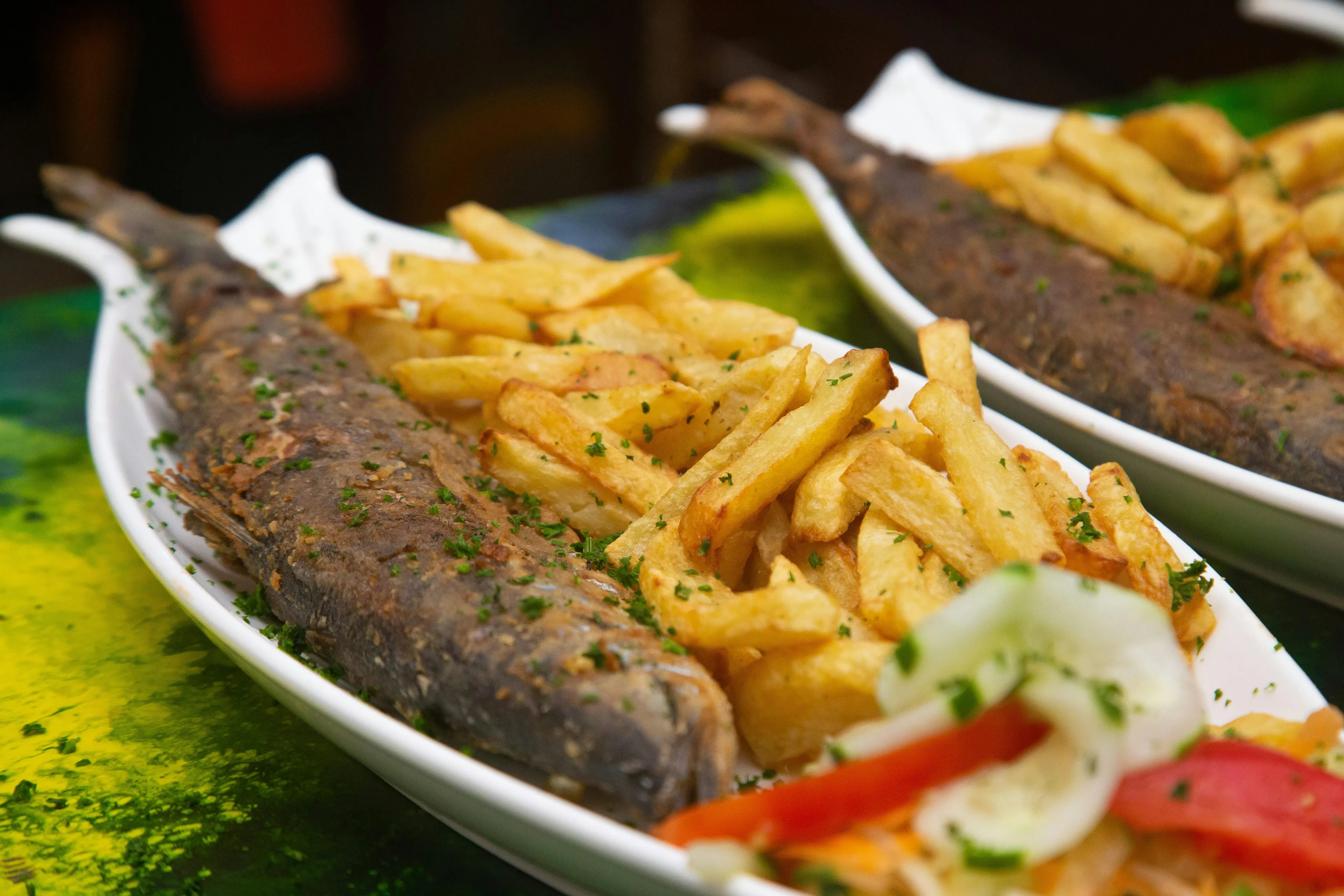 Two white fish-shaped dishes hold fish and chips with a side salad. This is a perfect meal.